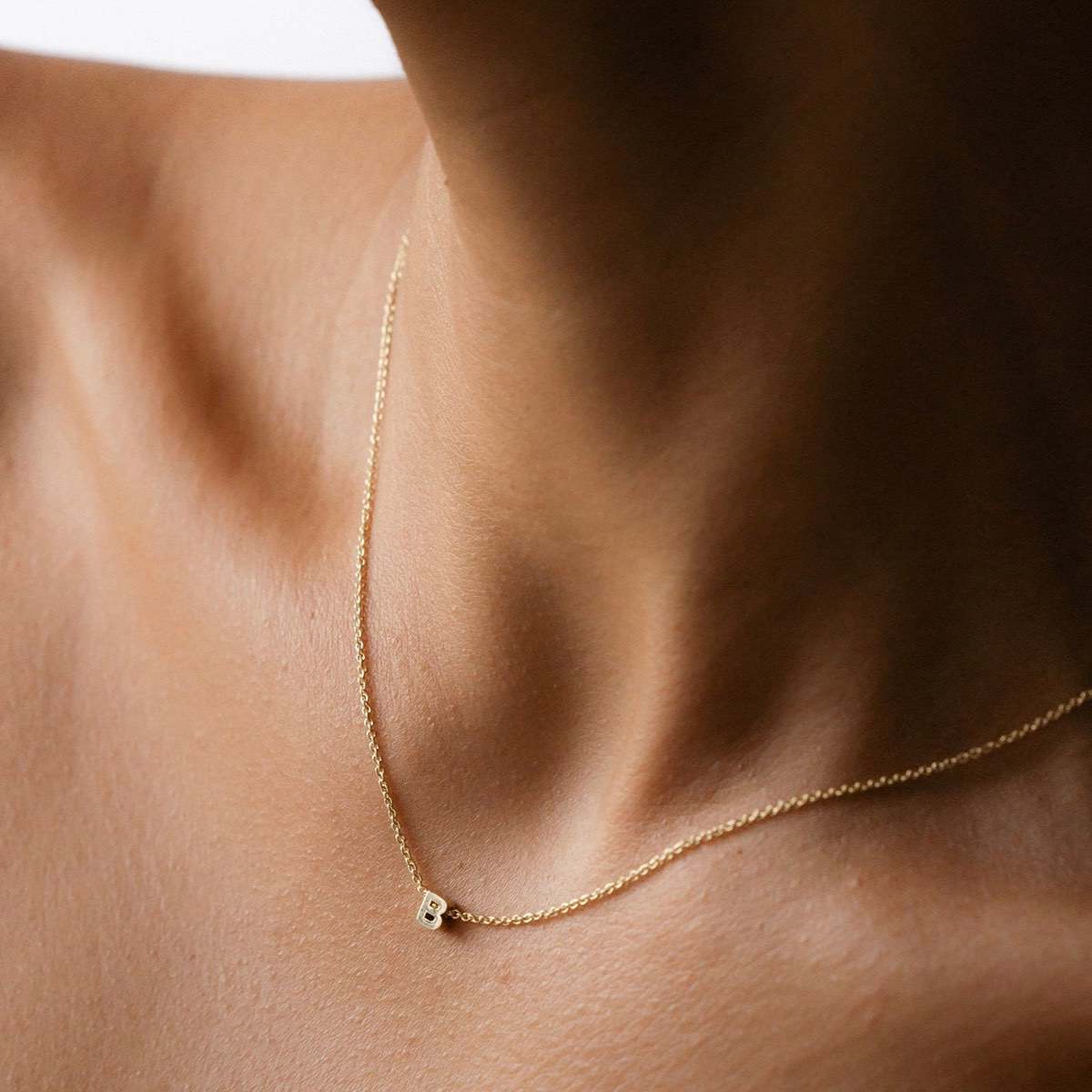  Hand finished solid gold letter necklace: Close up of a model wearing our beautiful 9ct yellow gold Tiny Letter B Charm Necklace with a 40cm cable chain