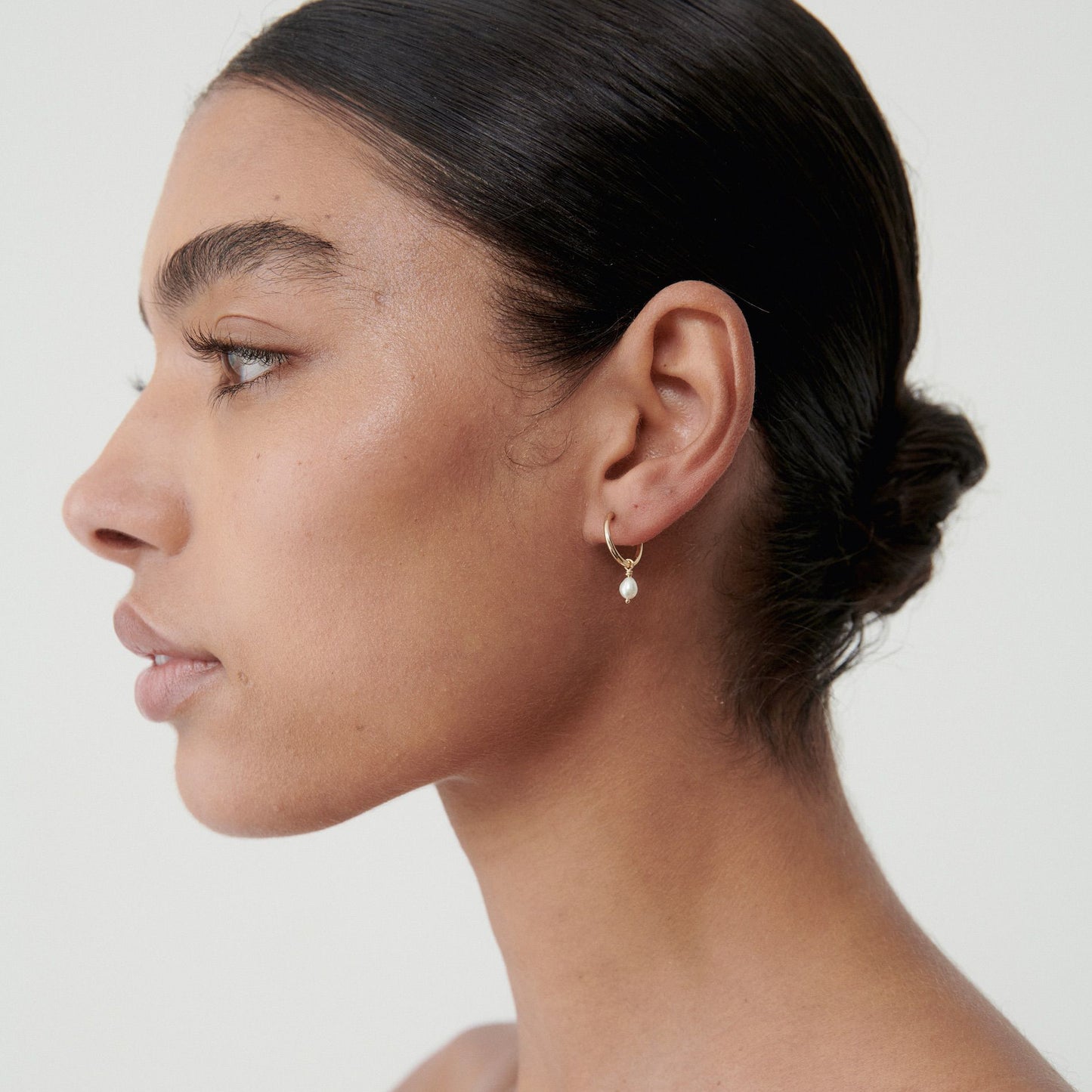 Woman wearing elegant gold dangling earrings with hair in a sleek bun. Minimalist luxury jewellery on a neutral background.