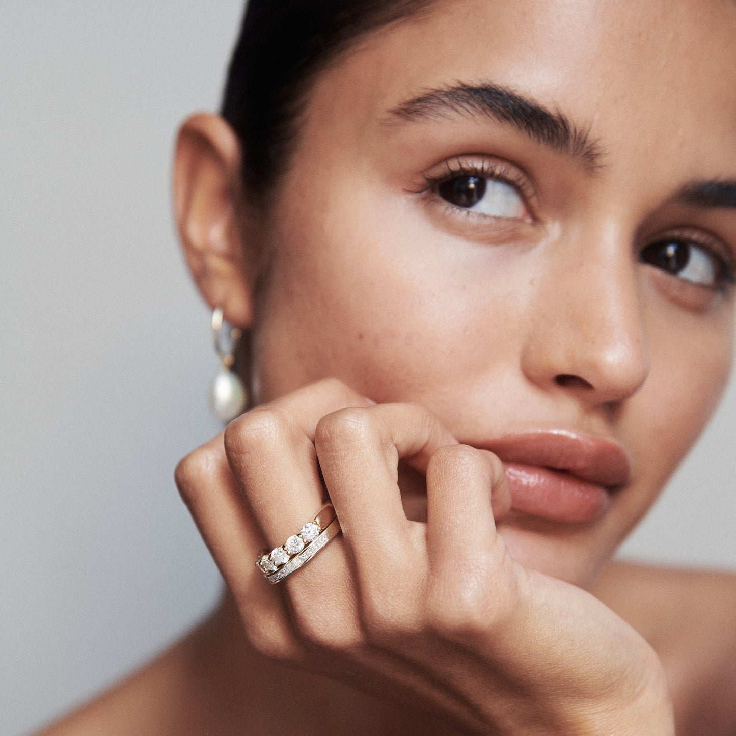 Woman showcasing diamond ring and pearl earring, gazing to the side. Elegant jewellery, luxury fashion, minimalist style.