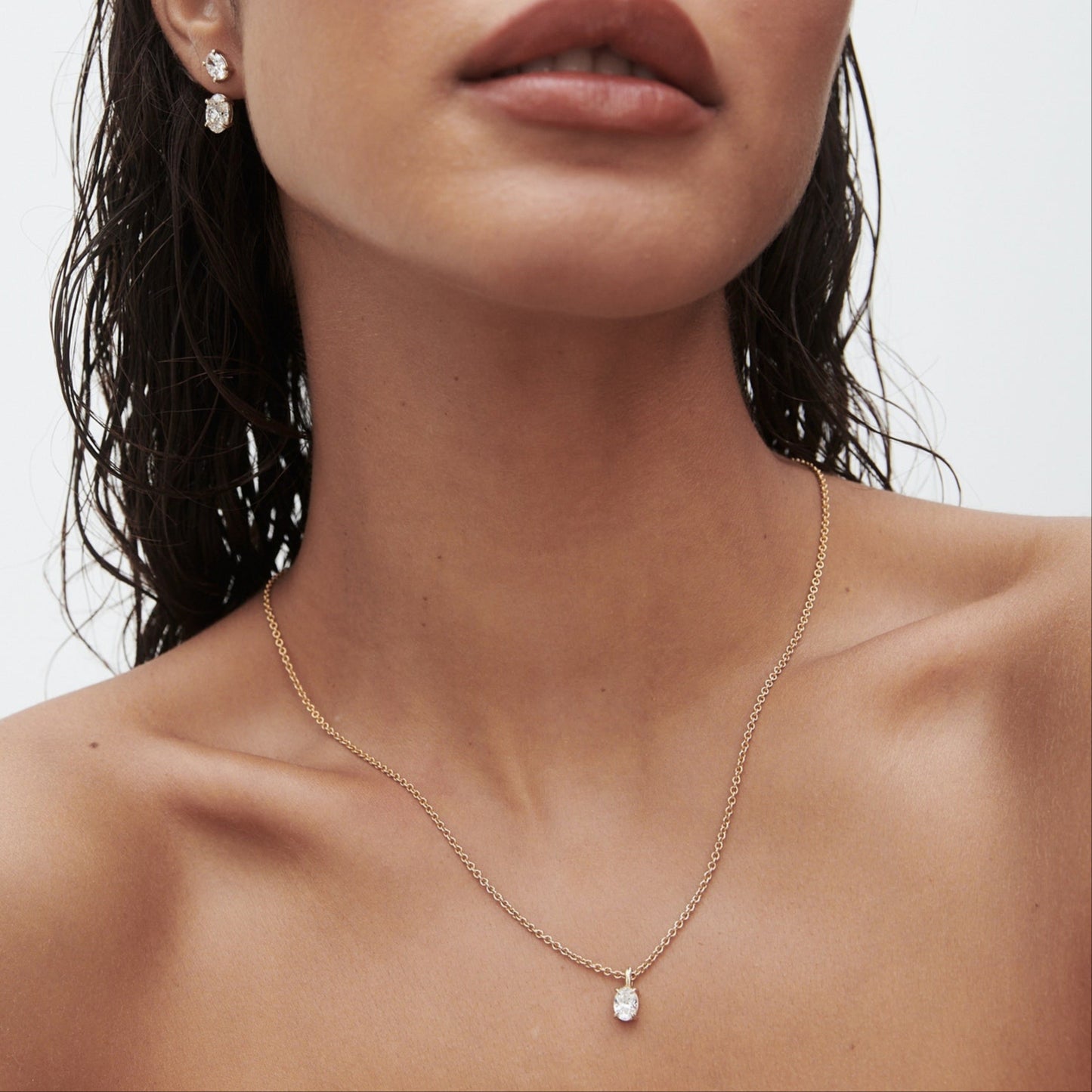 Woman with wet hair wearing a delicate gold necklace and matching earrings with a minimalist, elegant design.