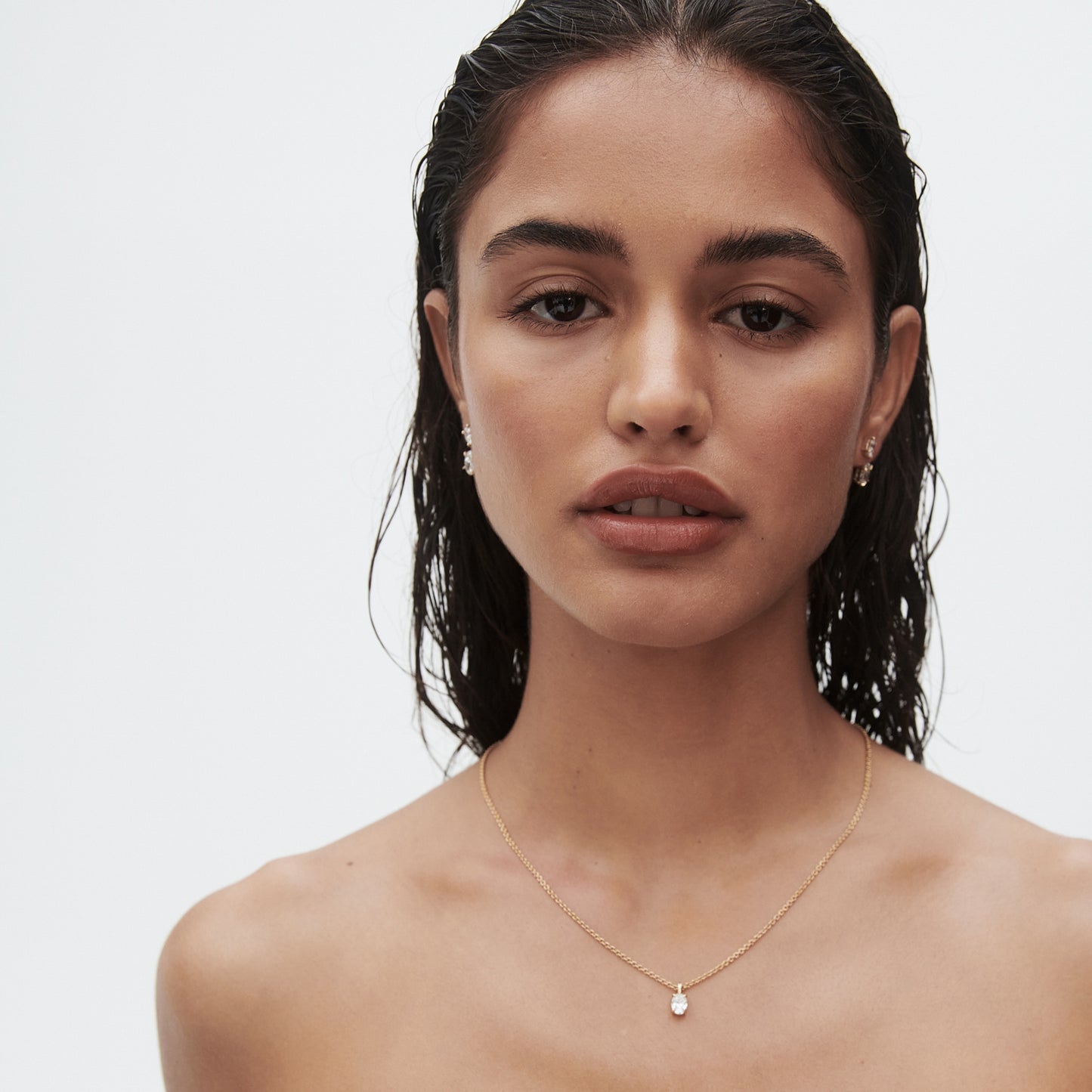 Woman with wet hair wearing a delicate gold necklace and matching earrings on a plain background, showcasing luxury jewellery.