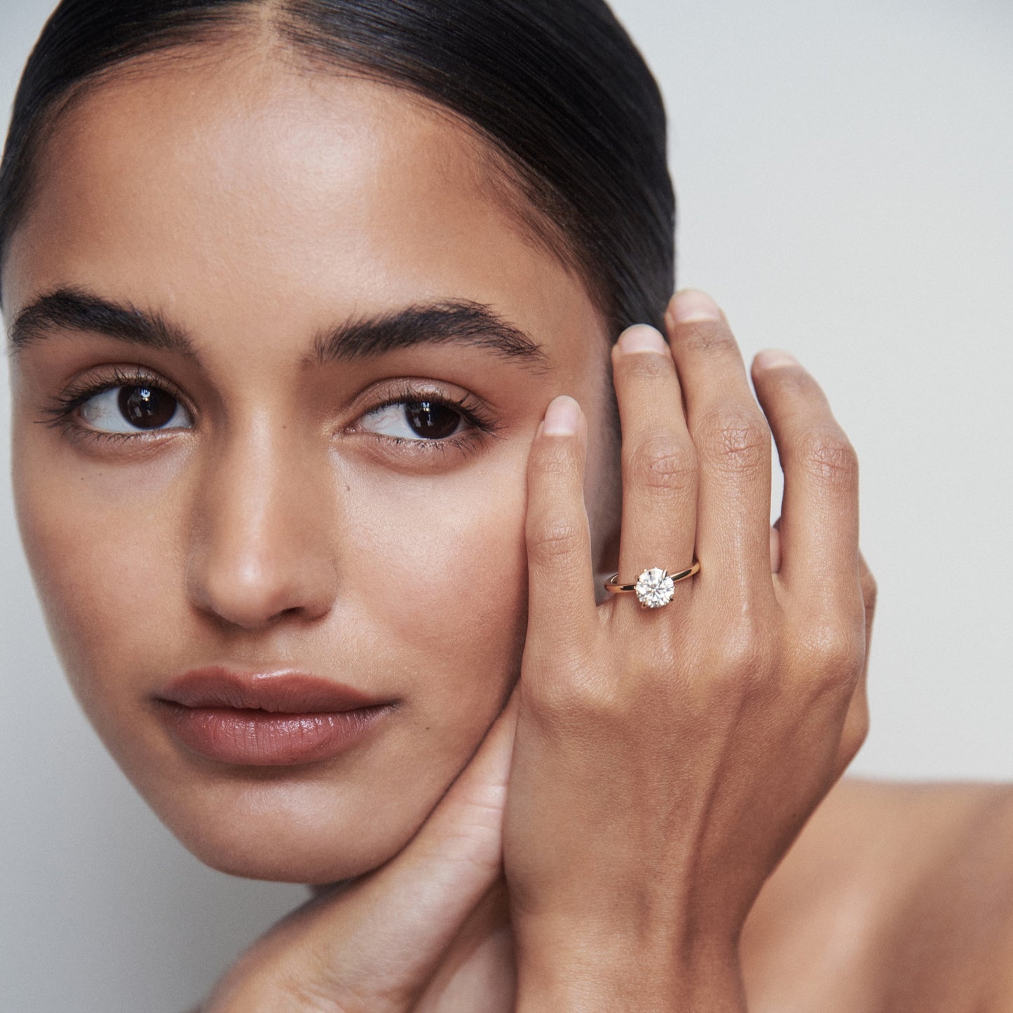 Woman showcasing a luxurious diamond ring on her finger, with a serene expression against a soft background. Elegant jewellery highlight.