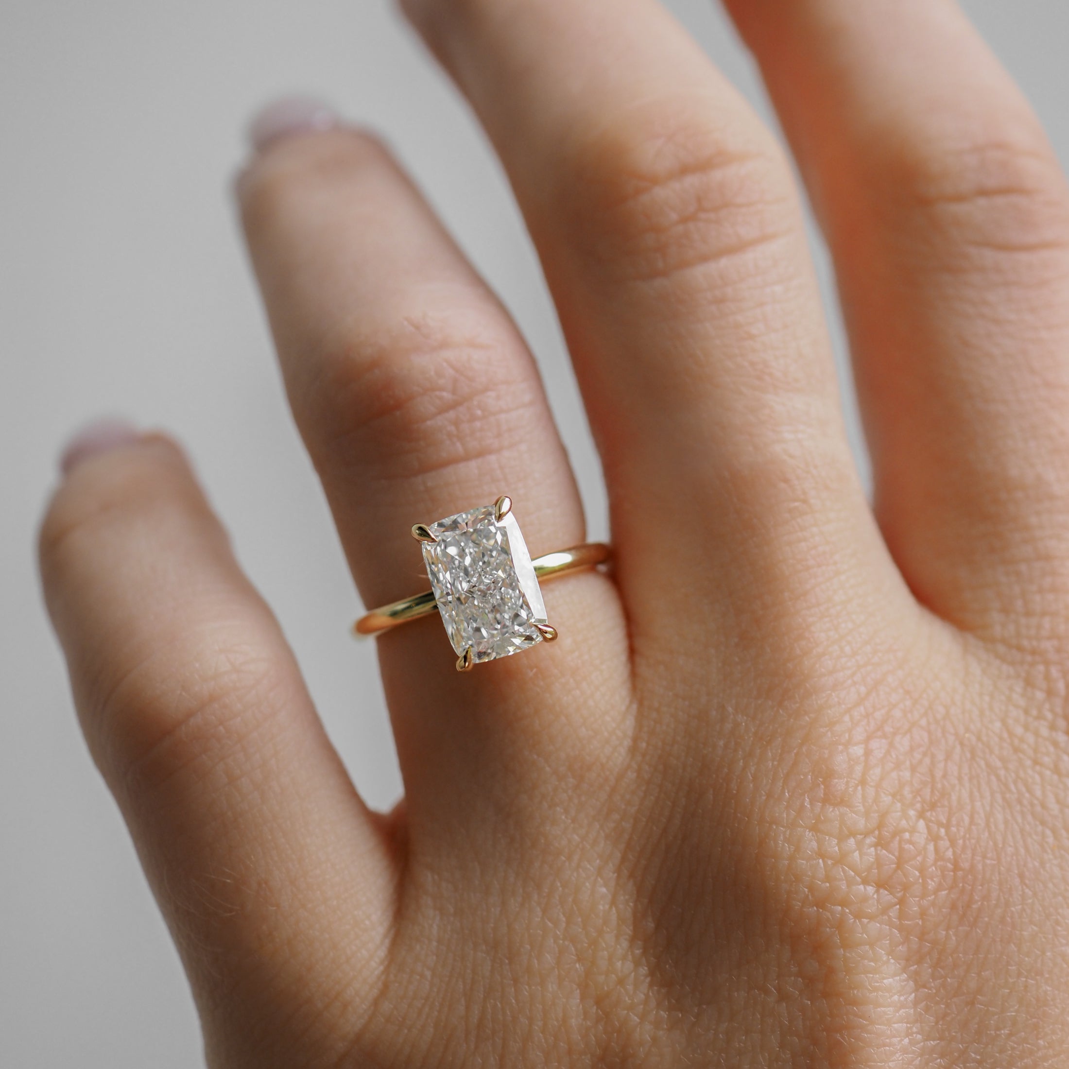 Hand wearing a luxury gold engagement ring with a large, rectangular diamond. Perfect for high-end jewellery enthusiasts.
