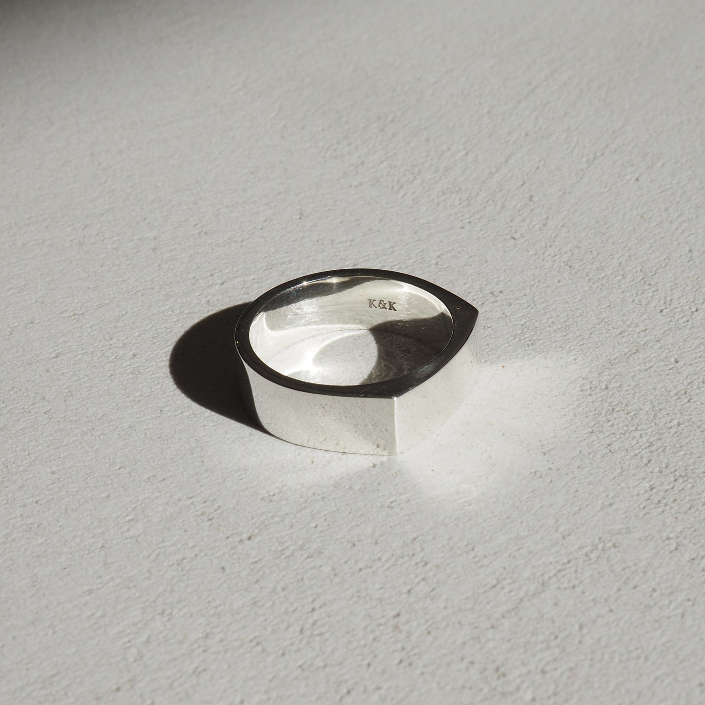 Minimalist silver ring with a modern, geometric design, casting a shadow on a light surface. Perfect for luxury jewellery enthusiasts.