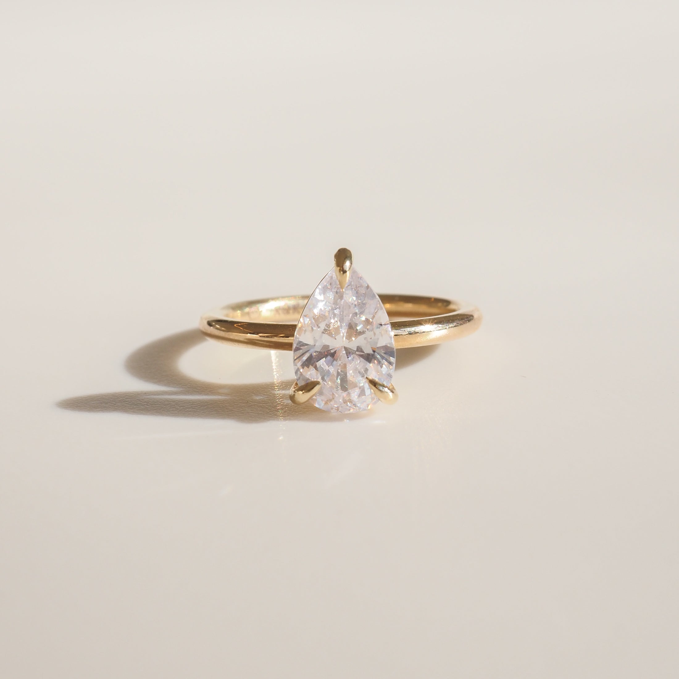 Gold ring with a large pear-shaped diamond, elegantly showcased on a light surface. Perfect for luxury jewellery enthusiasts.