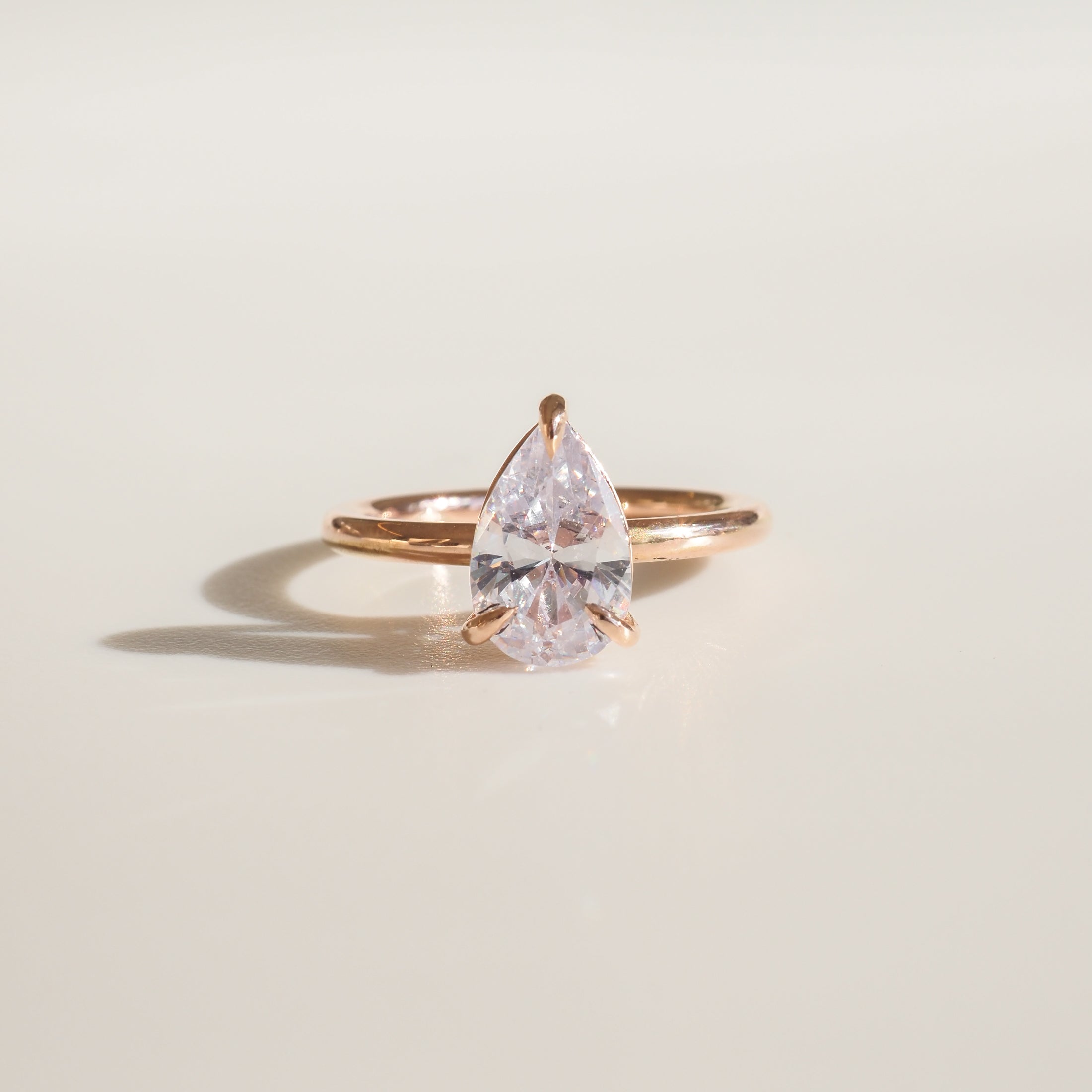Pear-shaped diamond ring set in elegant rose gold band, displayed on a smooth surface with soft lighting.