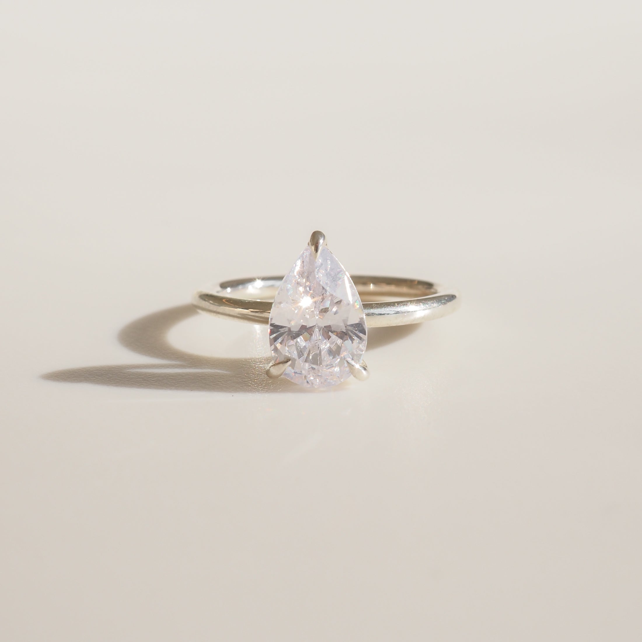 Pear-shaped diamond solitaire ring on a silver band, elegantly displayed on a light background.