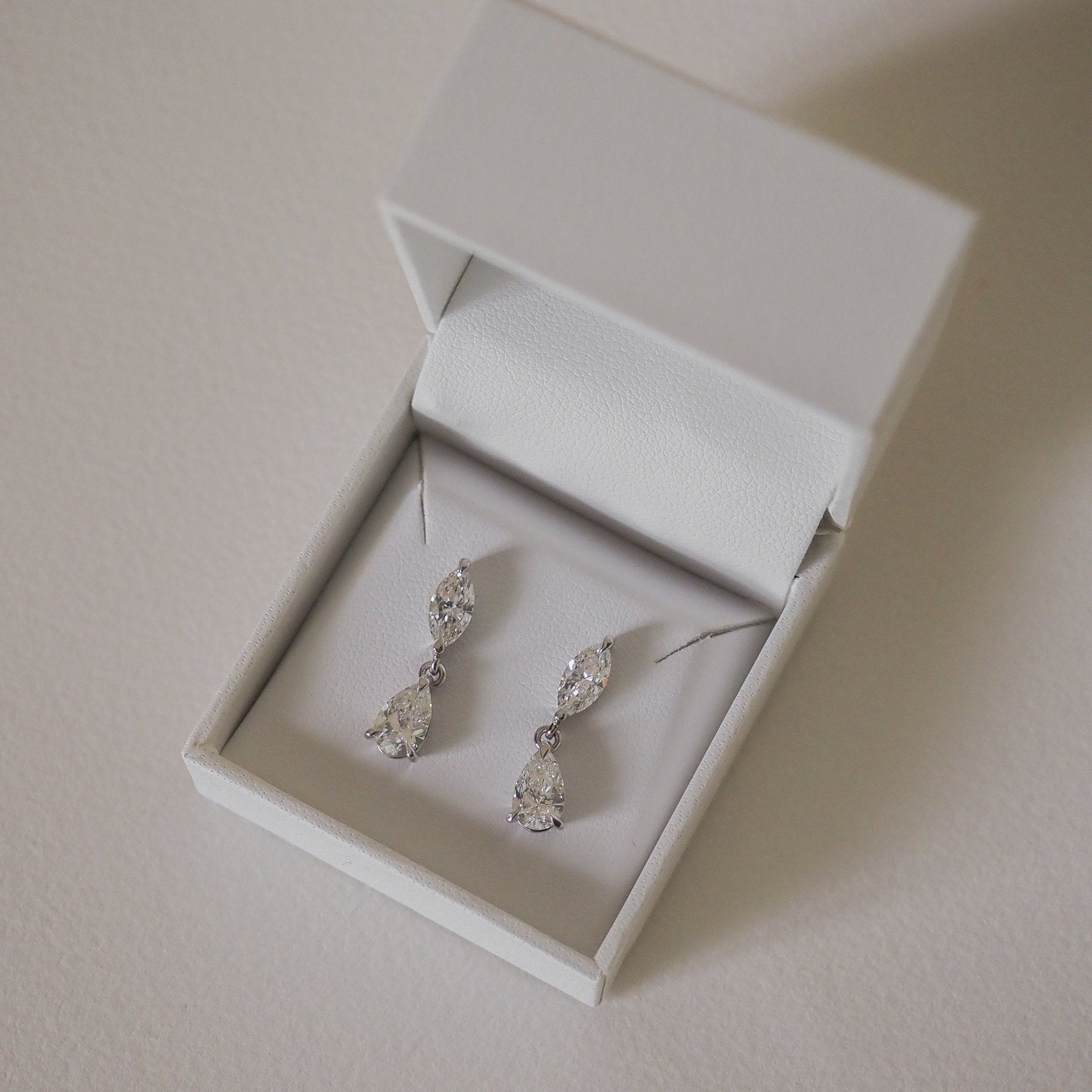 Elegant drop earrings with sparkling pear and marquise-cut gemstones in a white jewellery box; luxury accessories display.