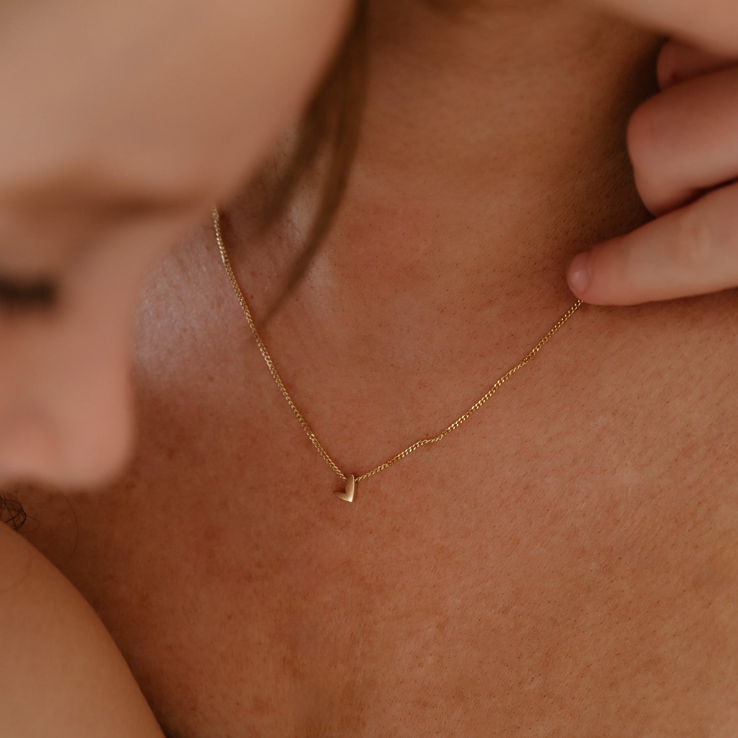 Close-up of a woman’s neck adorned with a delicate gold chain featuring a minimalist pendant, highlighting luxury jewellery elegance.