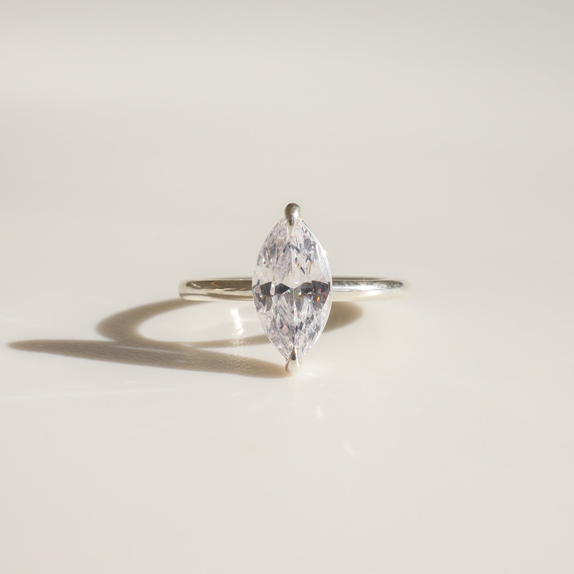 Elegant marquise diamond ring with a slim band, casting a soft shadow on a light background. Luxury jewellery design.