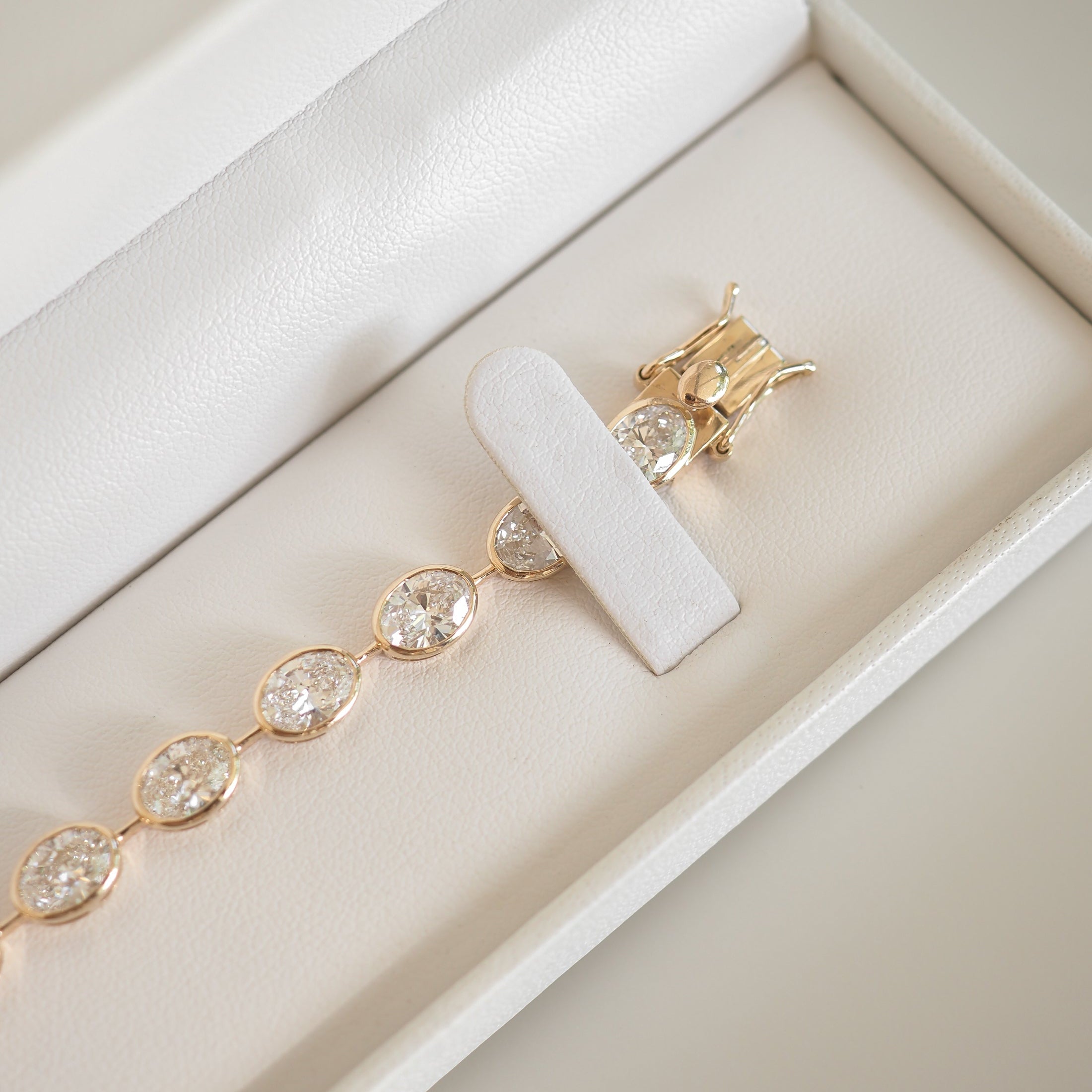 Gold bracelet with oval diamond settings in a white jewellery box. Luxurious and elegant, ideal for high-end fashion enthusiasts.
