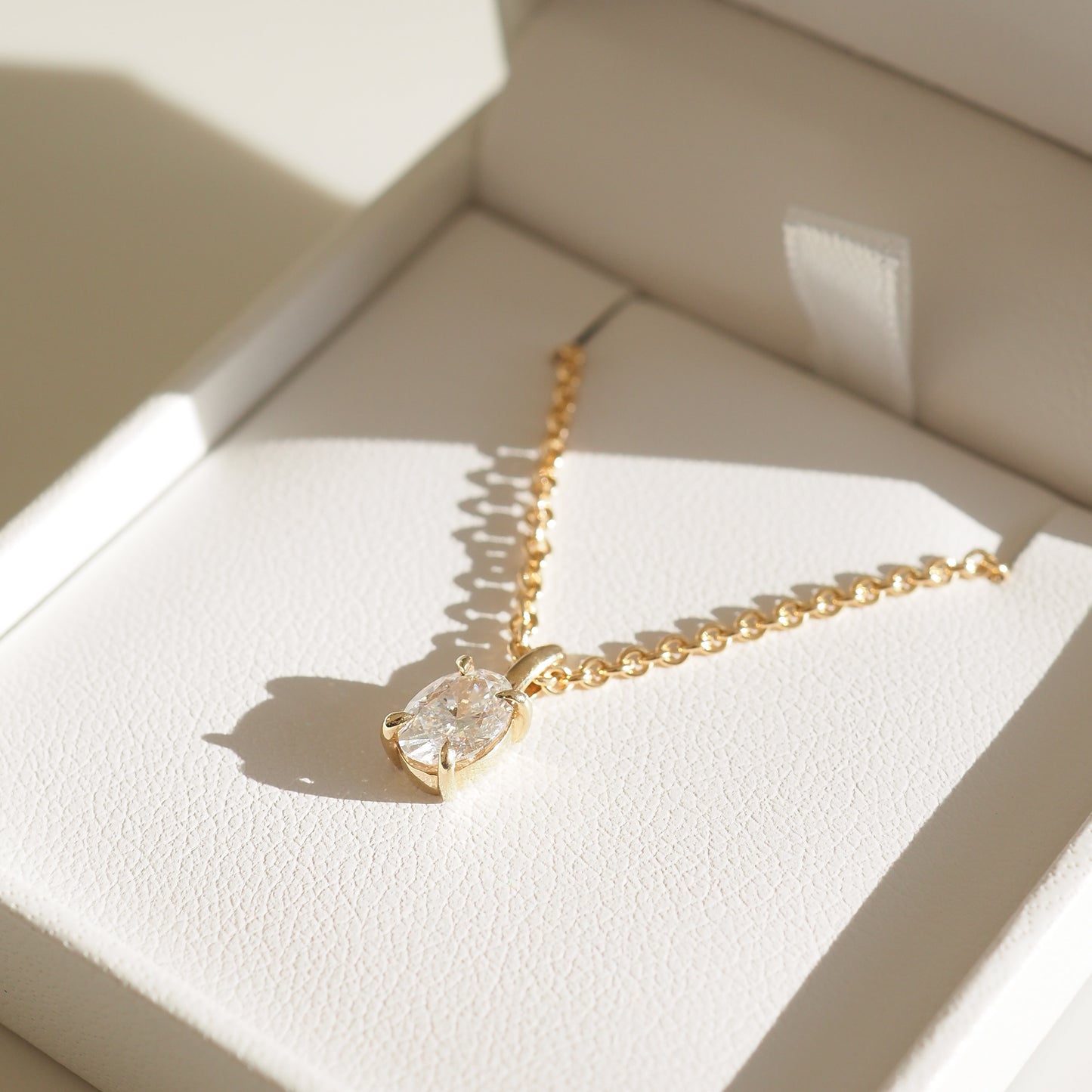 Gold chain necklace with an oval diamond pendant, elegantly presented in an open white jewellery box. Luxurious and radiant.