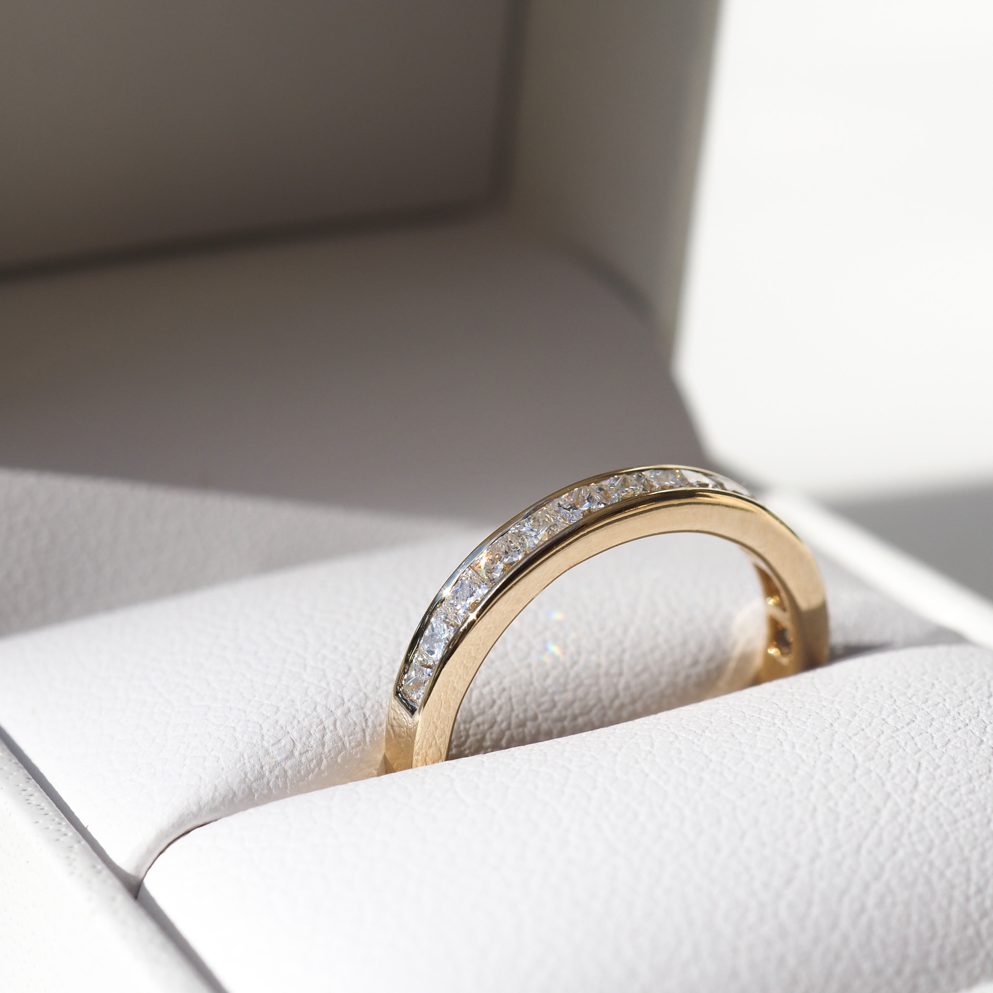 A gold wedding band with embedded diamonds rests elegantly in a white jewellery box, showcasing luxury design and craftsmanship.