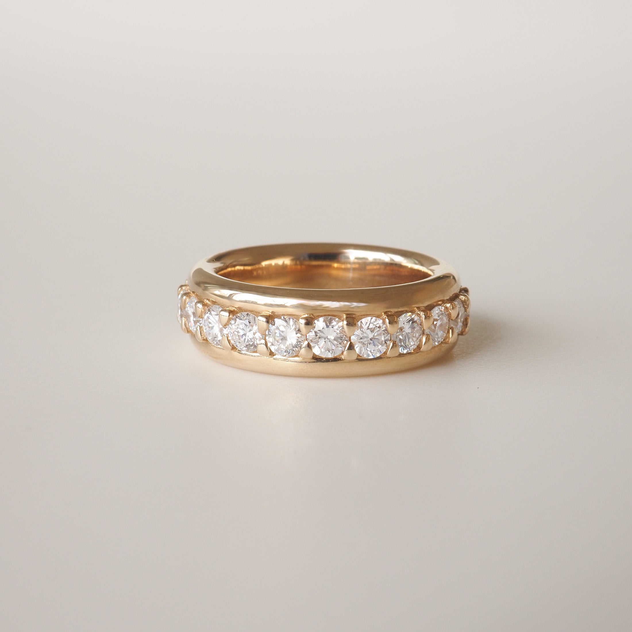 Gold ring with a row of sparkling diamonds set around the band, displayed on a plain background. Luxurious jewellery design.