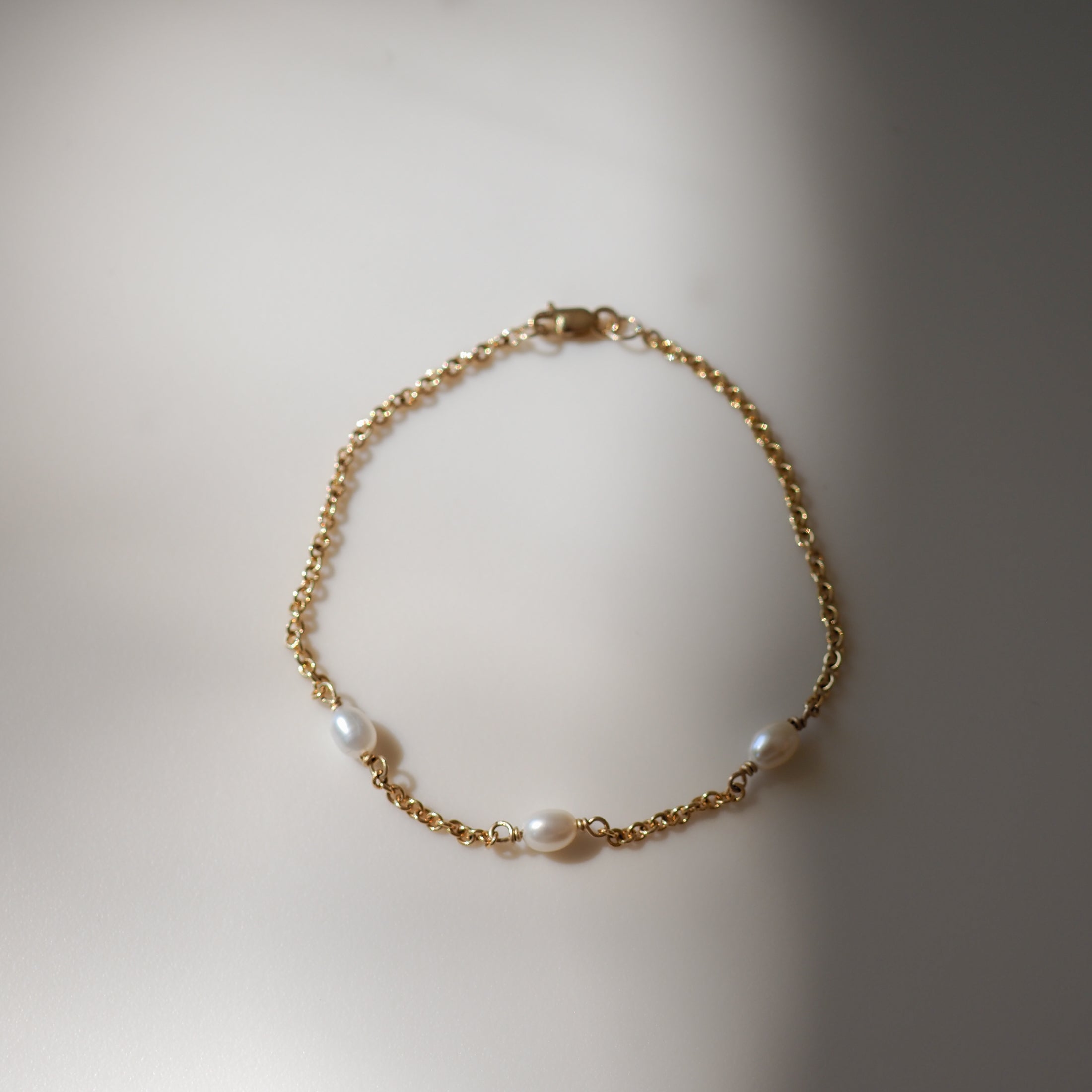 Elegant gold chain bracelet with three freshwater pearls, beautifully laid out on a soft, light surface.