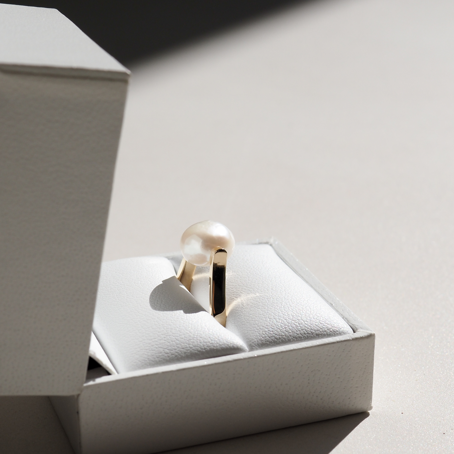 Elegant pearl ring in a white jewellery box, showcasing luxury design. Perfect lighting highlights its high-end allure and gold band.