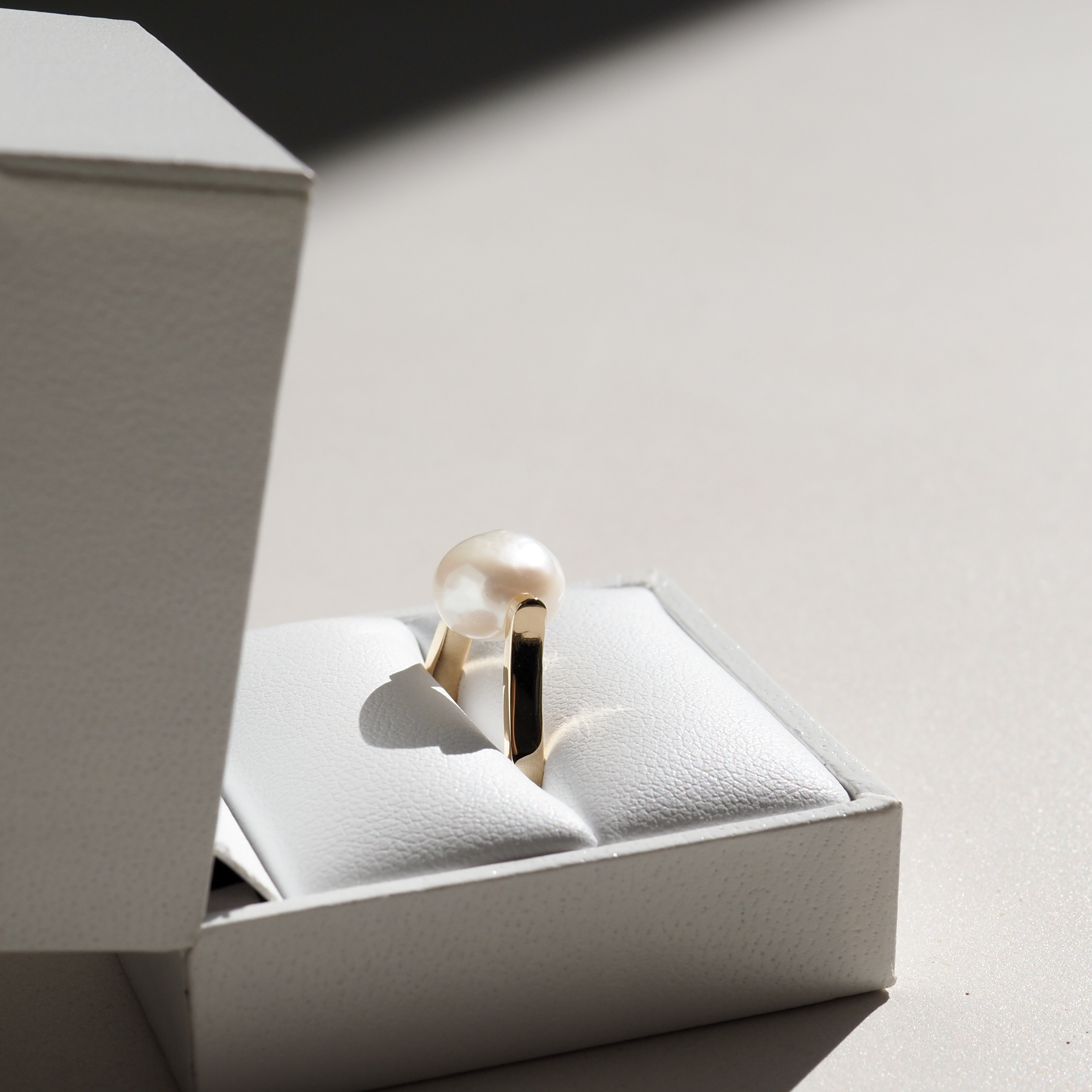 Elegant pearl ring in a white jewellery box, showcasing luxury design. Perfect lighting highlights its high-end allure and gold band.