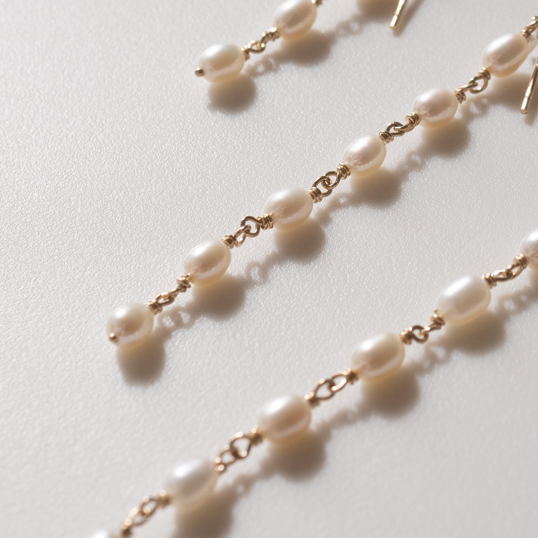 Delicate pearl earrings draped on a neutral background, linked by fine gold chains, embodying luxury and elegance in jewellery design.