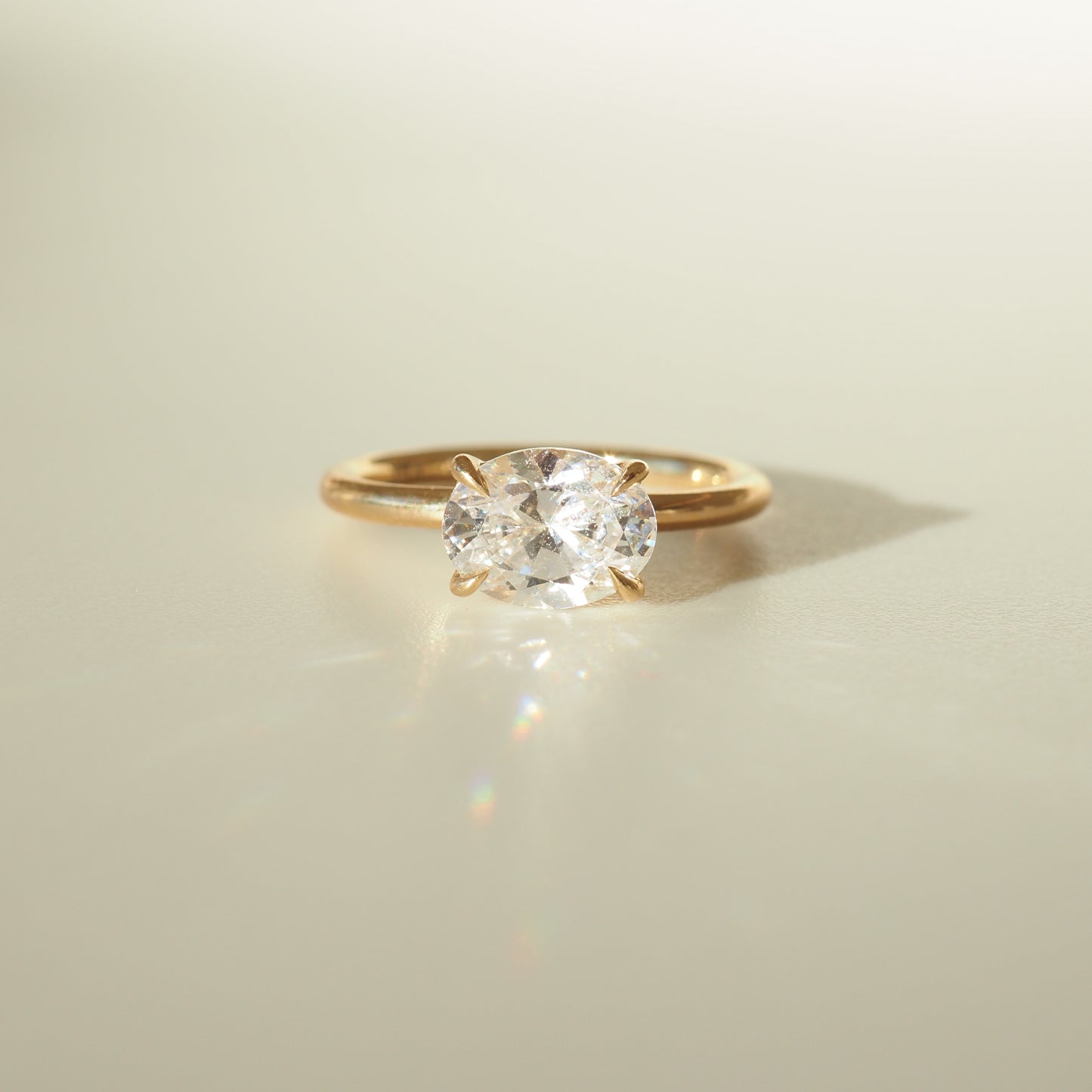 Gold ring with a large oval diamond solitaire, elegantly displayed on a softly lit surface, casting a subtle shadow.