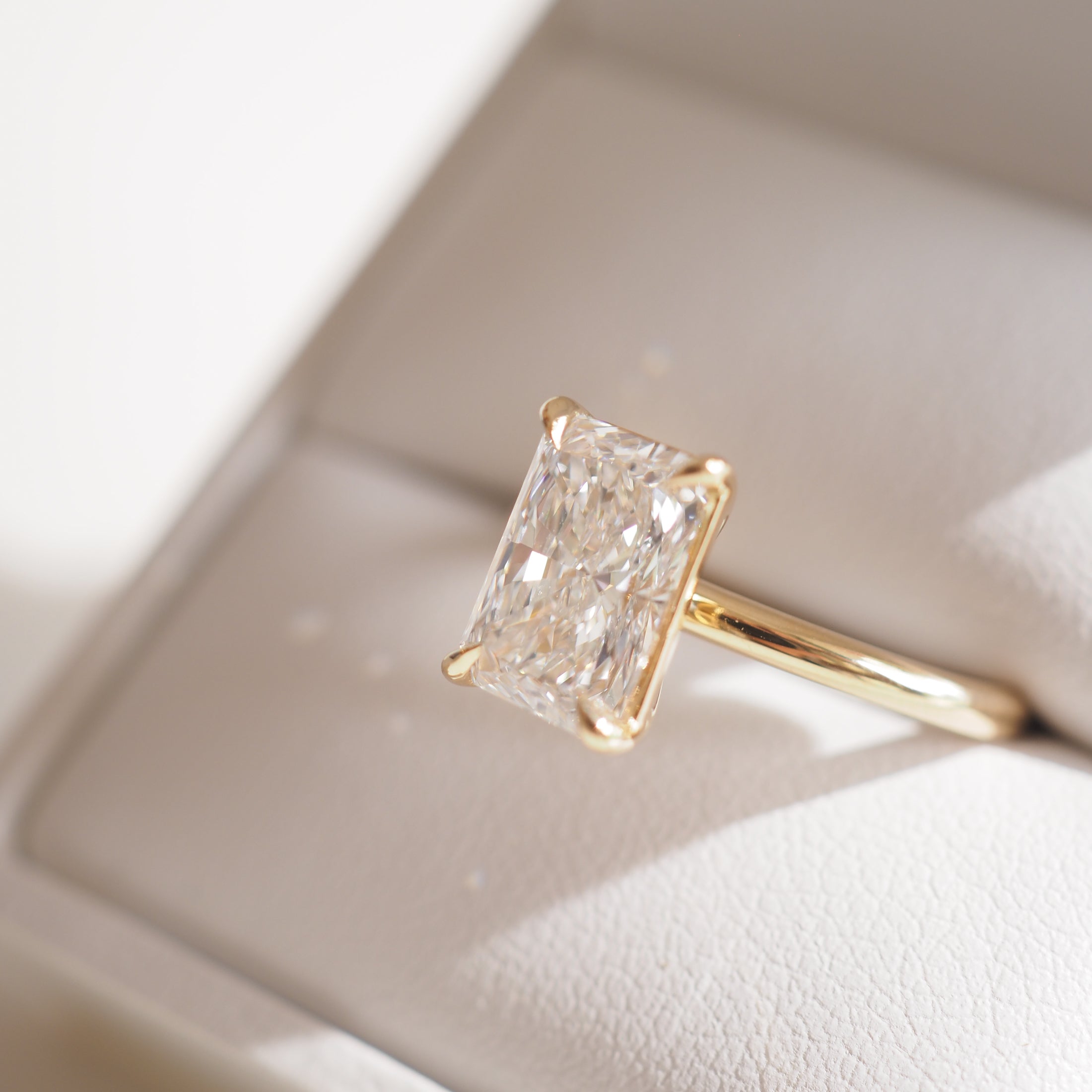 Gold ring with a large emerald-cut diamond in a white box. Luxurious jewellery, ideal for engagements or special occasions.
