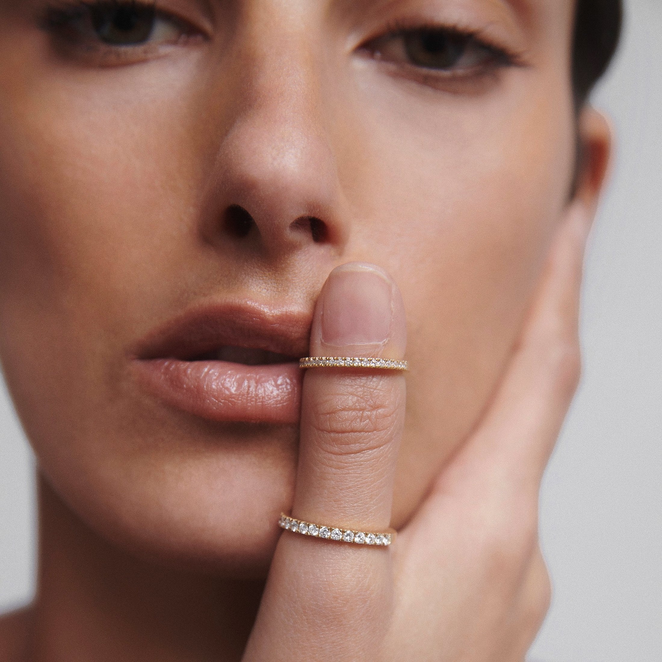 Woman with two diamond rings on finger, posing thoughtfully with hand on face. Luxury jewellery close-up.