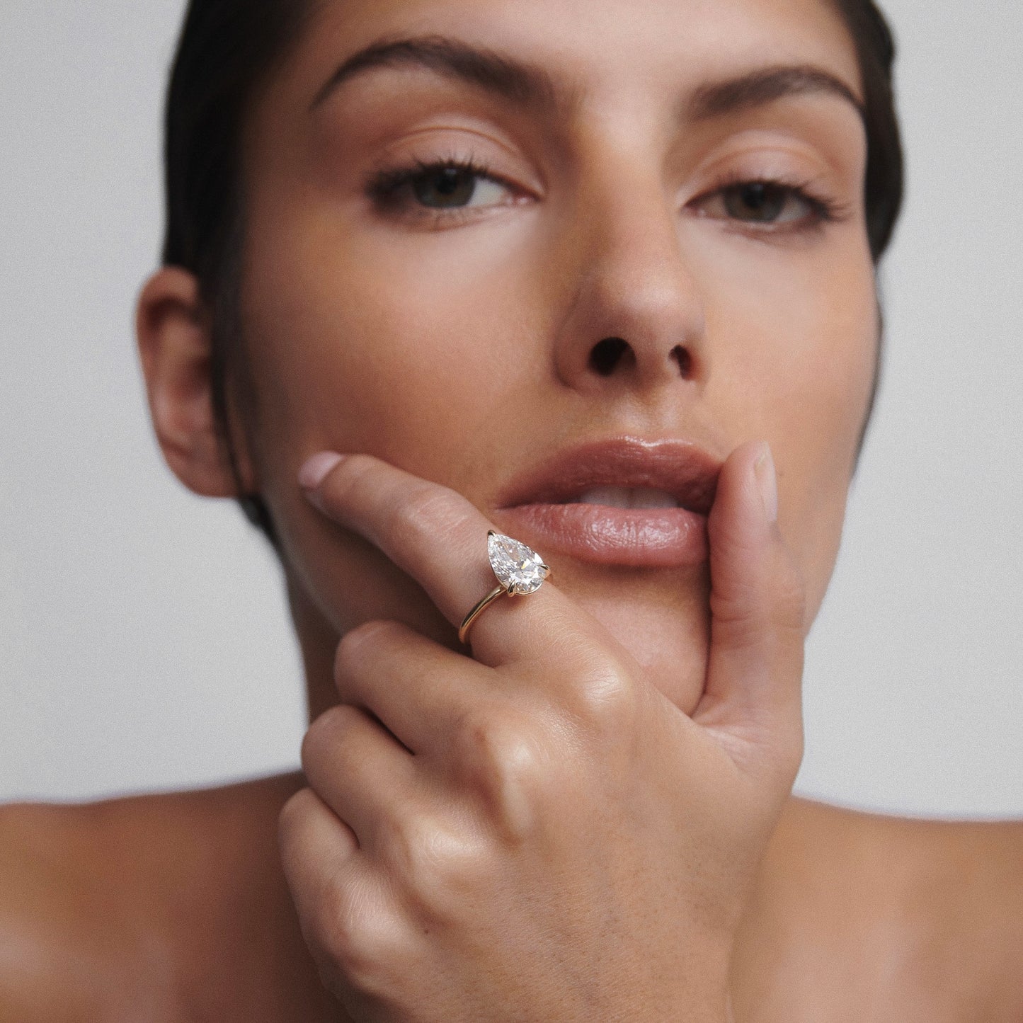 Close-up of a person wearing a gold ring with a large pear-shaped diamond, resting their chin on their hand, showcasing luxury jewellery.
