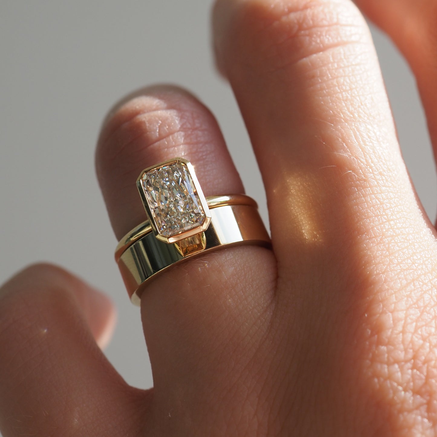 Close-up of a hand wearing a luxurious gold ring with a large, rectangular diamond, reflecting light. Perfect for emphasising high-end jewellery.