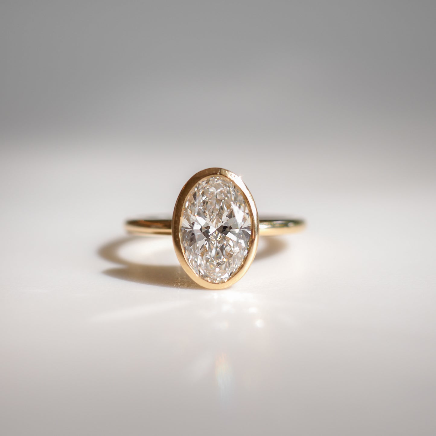 Gold ring featuring a prominent oval diamond, elegantly displayed on a reflective surface, evoking luxury and sophistication in fine jewellery.