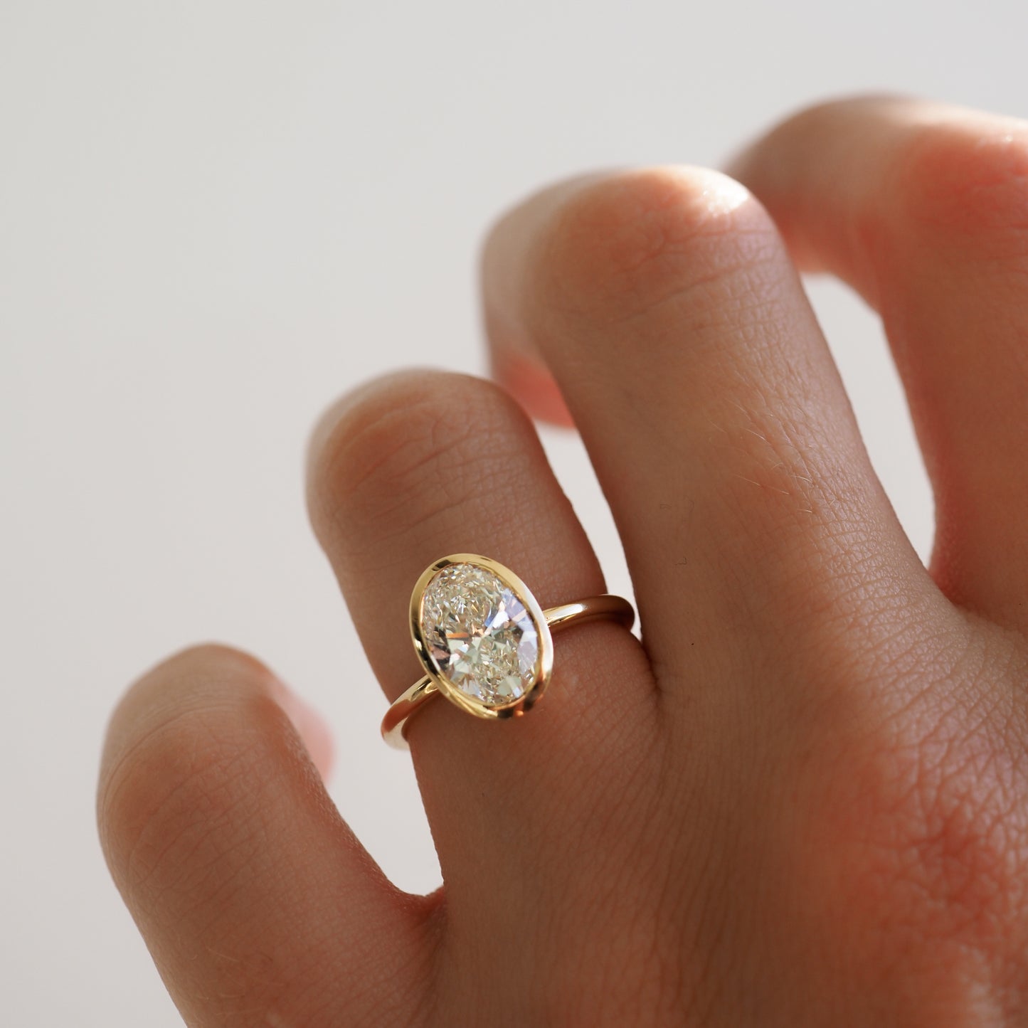 A hand wearing an elegant gold ring with a large oval diamond, showcasing luxury jewellery design against a soft, blurred background.