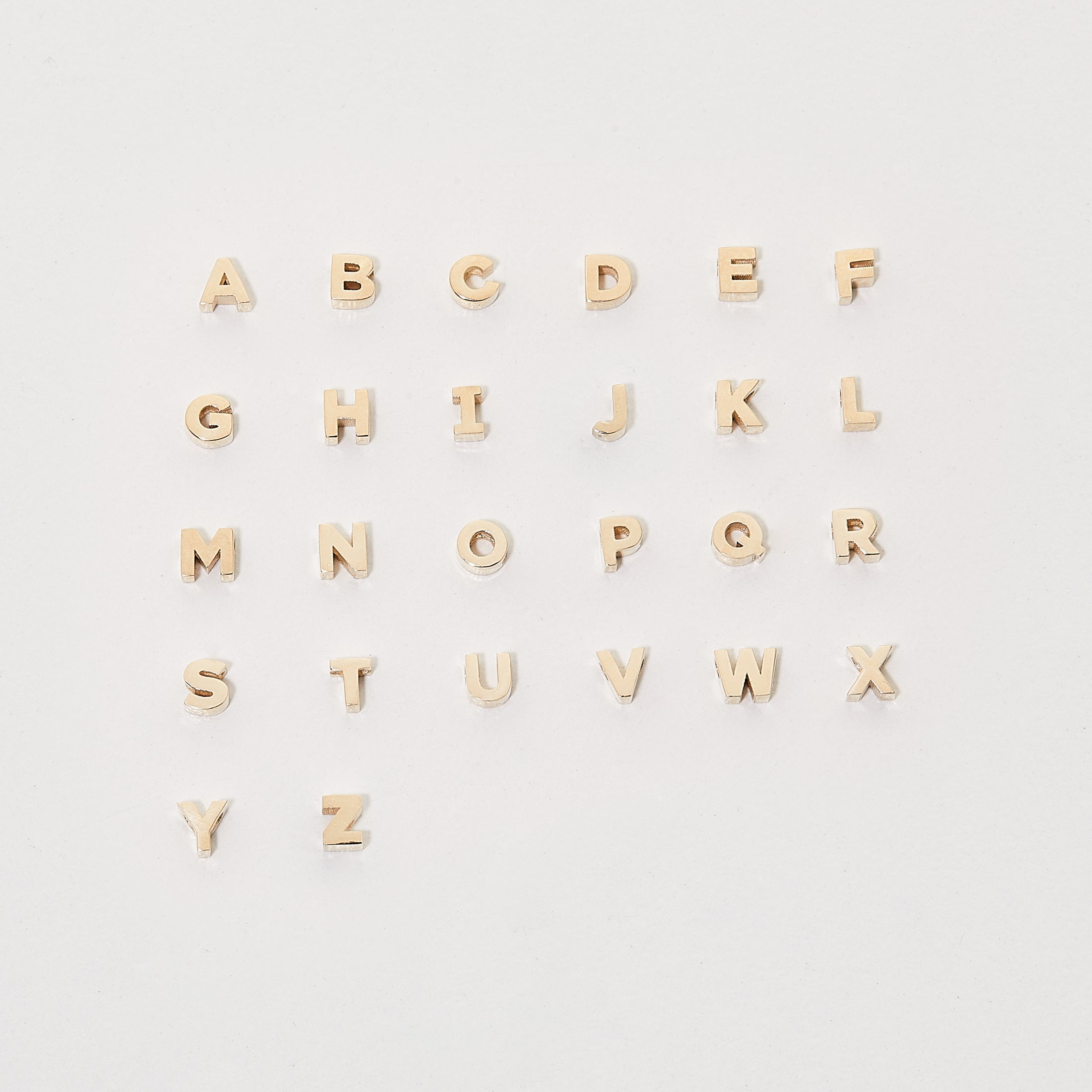 Gold alphabet pendant charms arranged alphabetically on a white background, showcasing luxury jewellery design.
