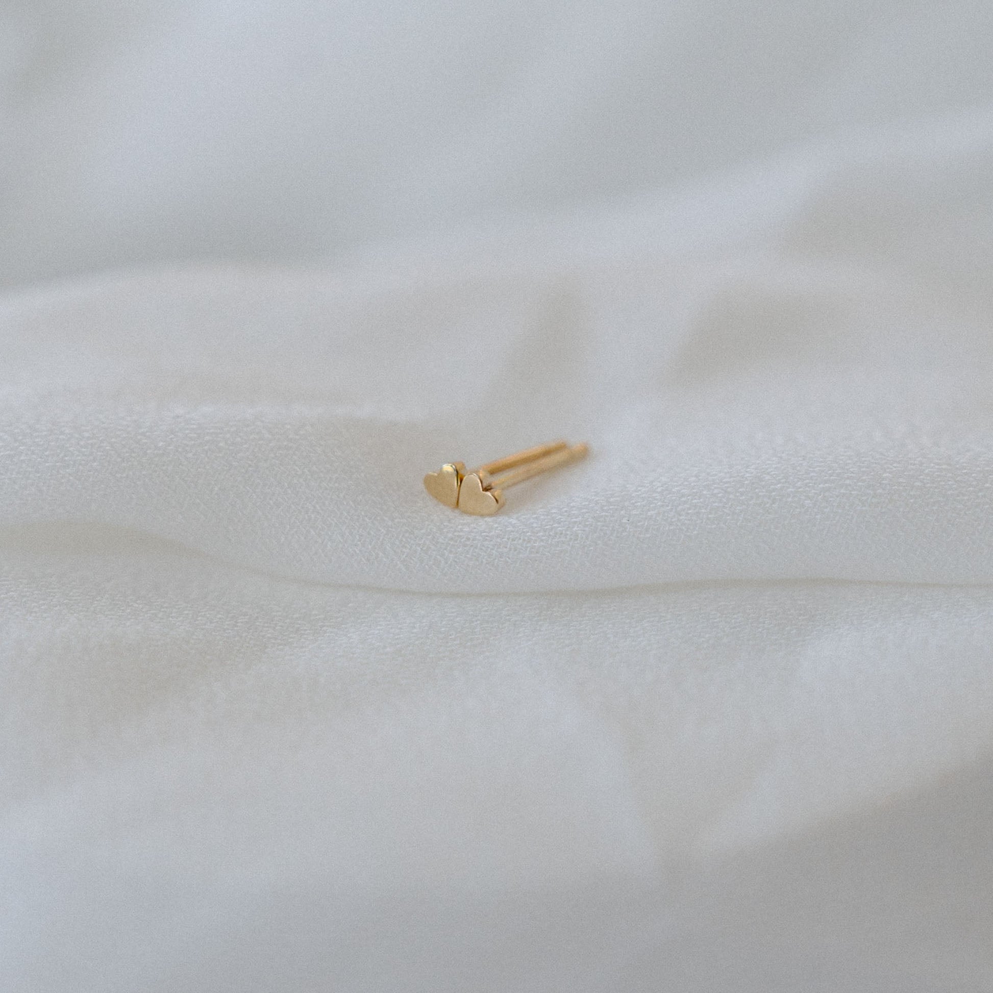 Elegant gold stud earring in a heart shape resting on soft, white fabric, highlighting intricate jewellery design and luxury aesthetic.