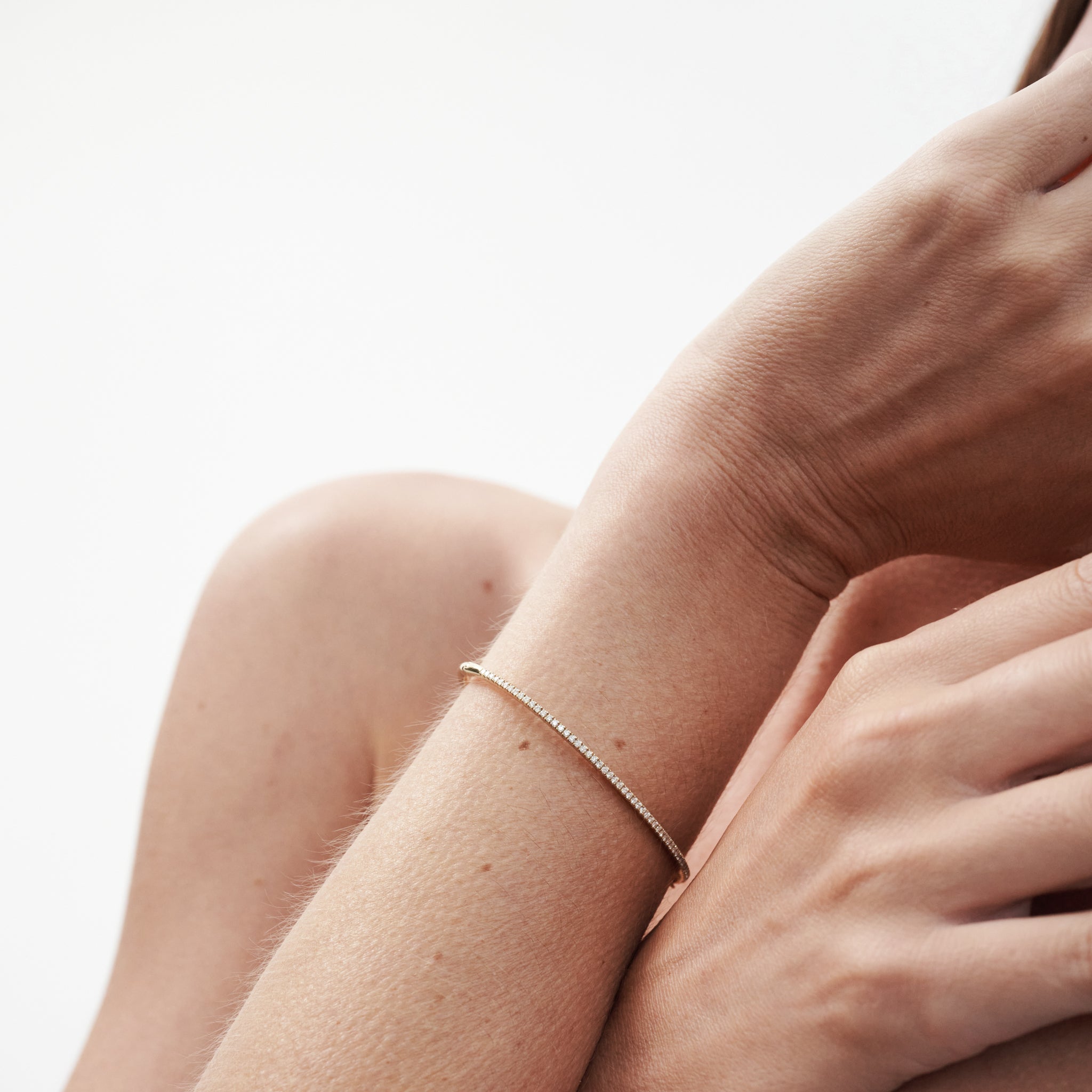 Close-up of a woman's arm adorned with a minimalist gold bracelet, showcasing elegant luxury jewellery against a neutral background.