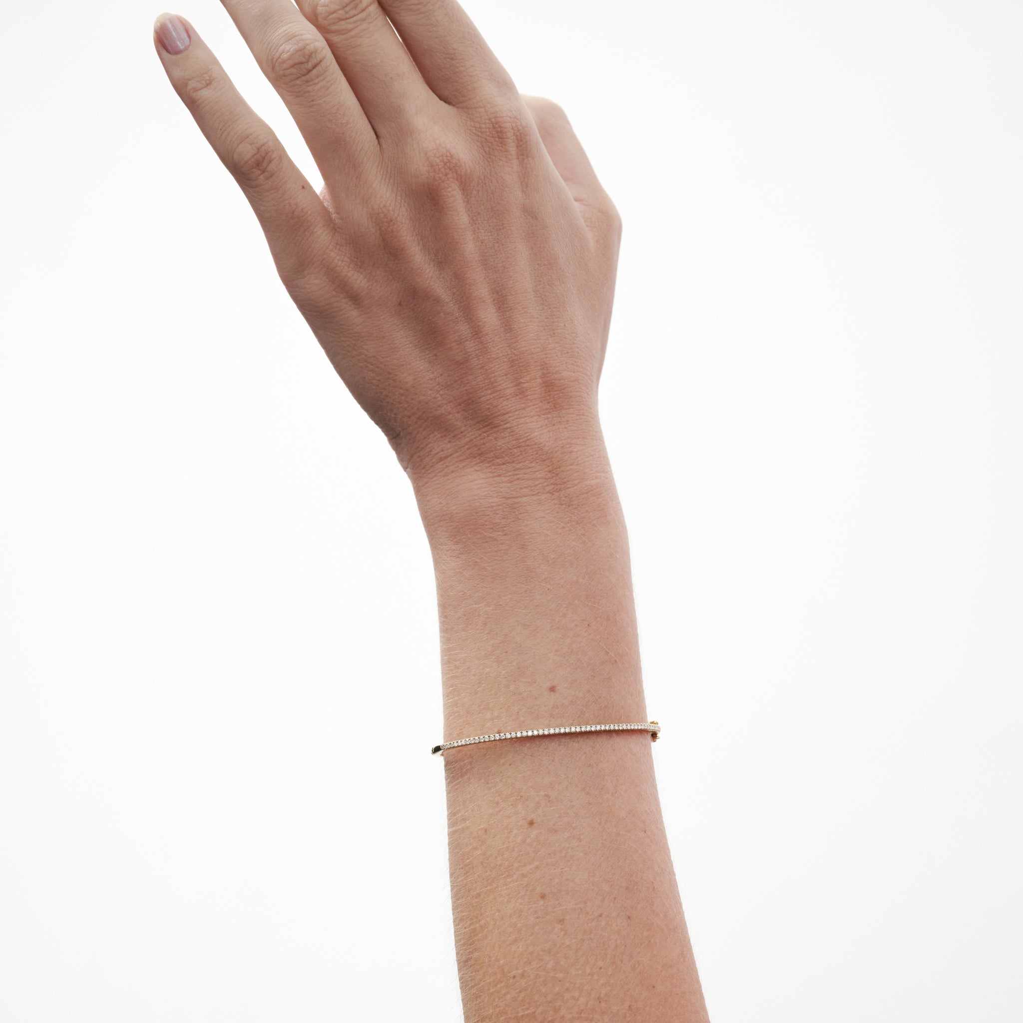 Hand wearing a minimalist gold bracelet against a plain background. The bracelet subtly catches the light, exuding elegance and simplicity.