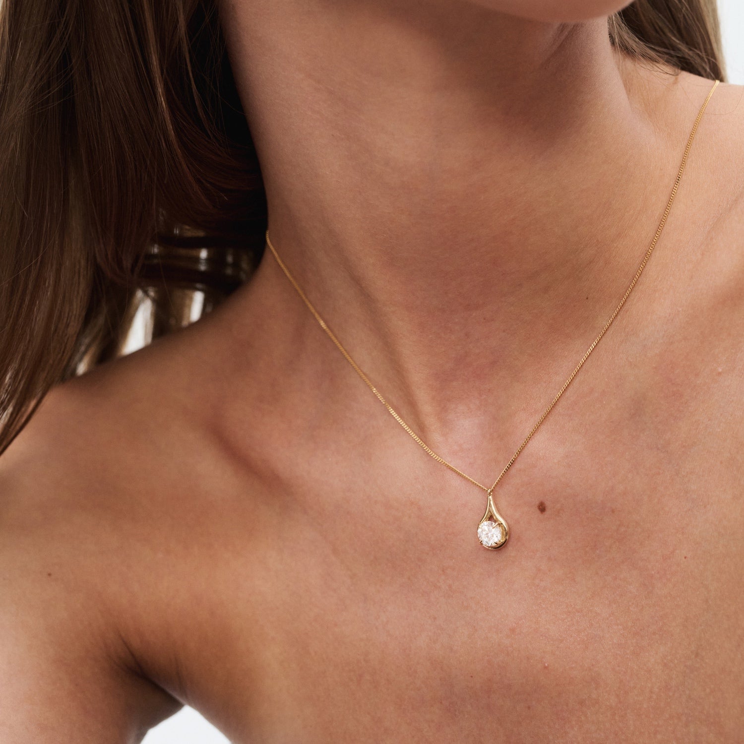 Close-up of a woman's neck adorned with a gold necklace featuring a single sparkling diamond pendant, epitomising luxury jewellery elegance.