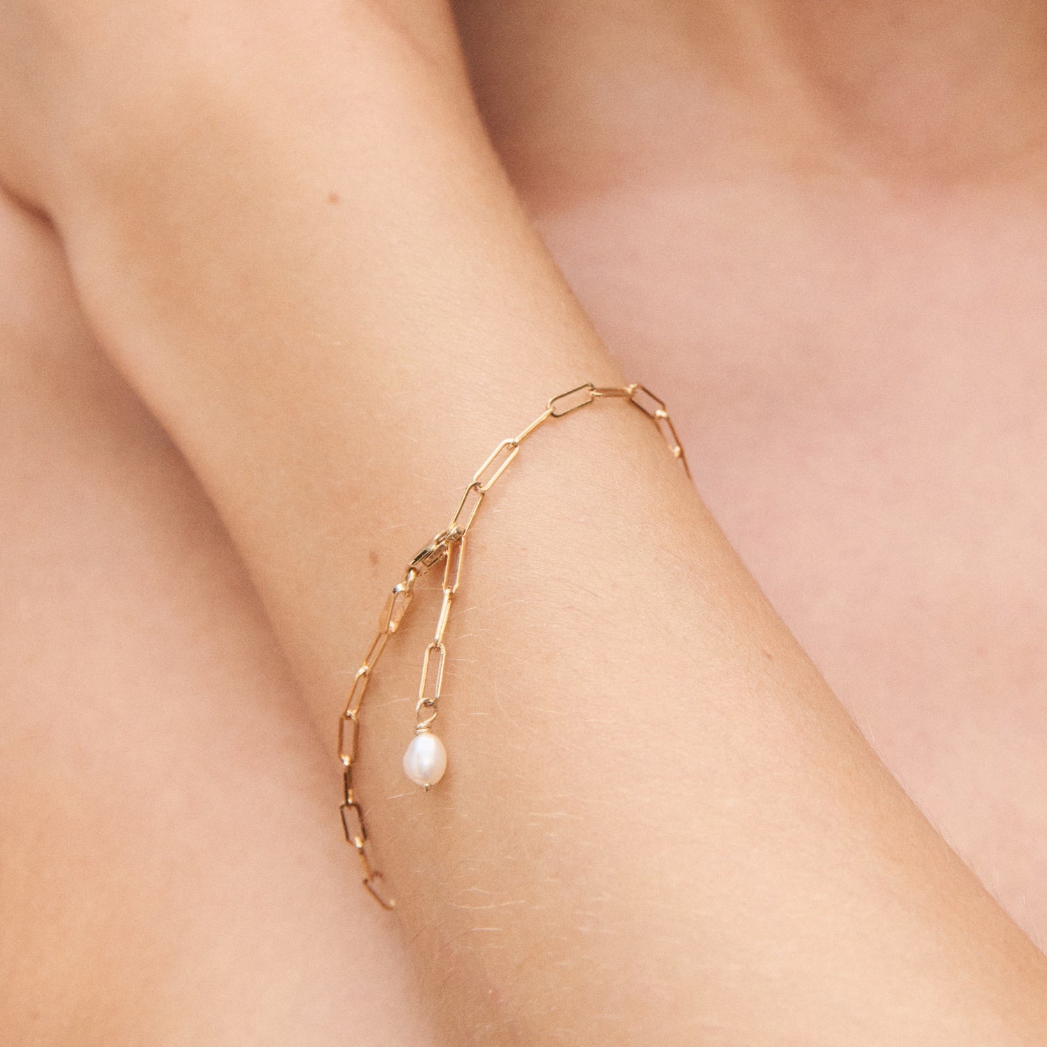 Elegant gold chain bracelet with small pearl detail, worn on wrist. Luxurious, minimalist design perfect for high-end jewellery enthusiasts.