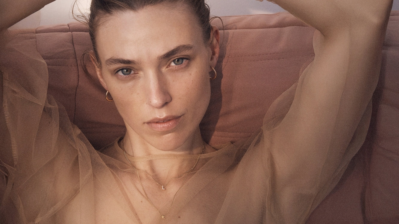 Woman sitting on a couch wearing Kate & Kole jewellery including hoops, diamond letter necklace and tiny letter necklace.