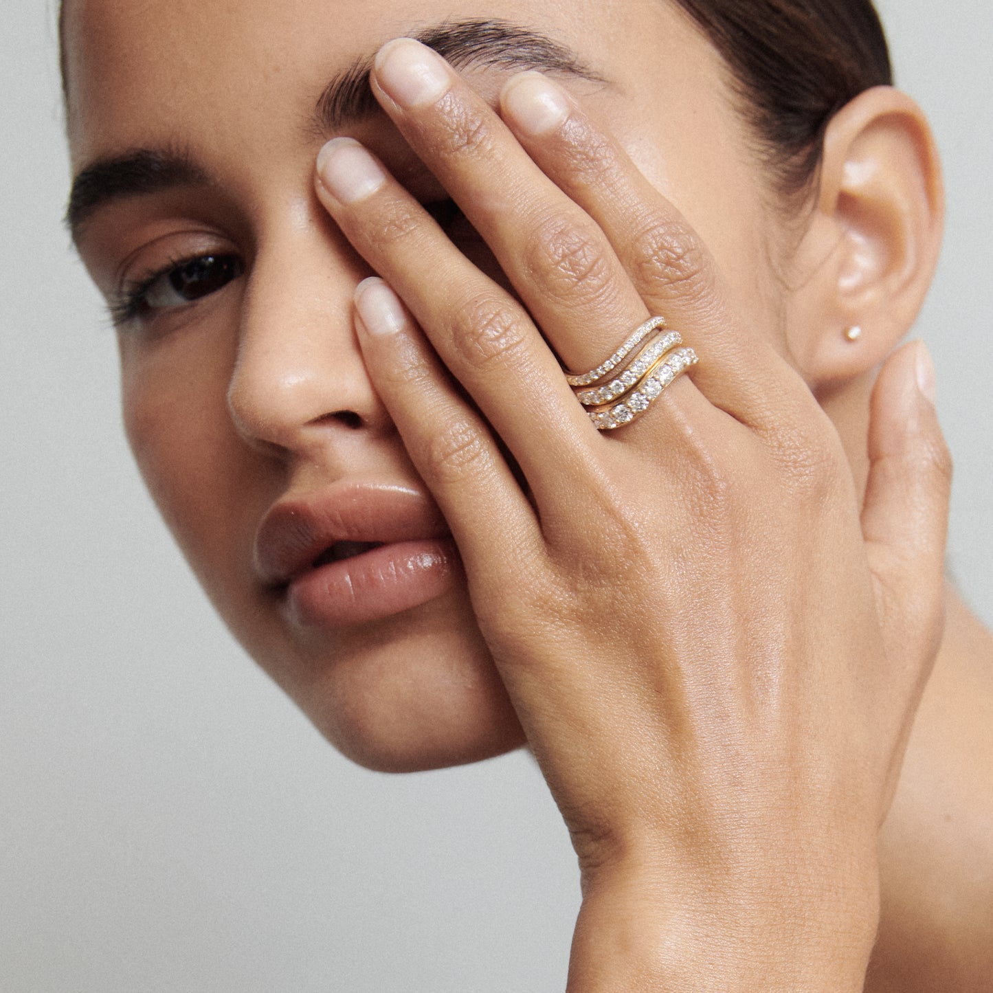 Woman showcasing gold and diamond rings on her fingers, covering half of her face. Elegant and luxurious jewellery display.