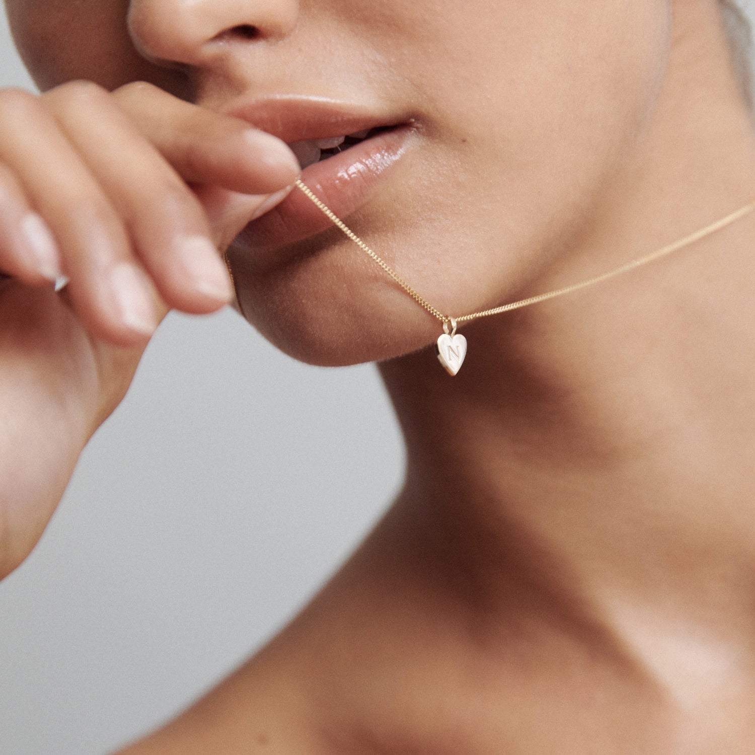 Close-up of a woman's hand holding a gold necklace with a small heart pendant near her lips. Luxurious jewellery, elegance, and style.