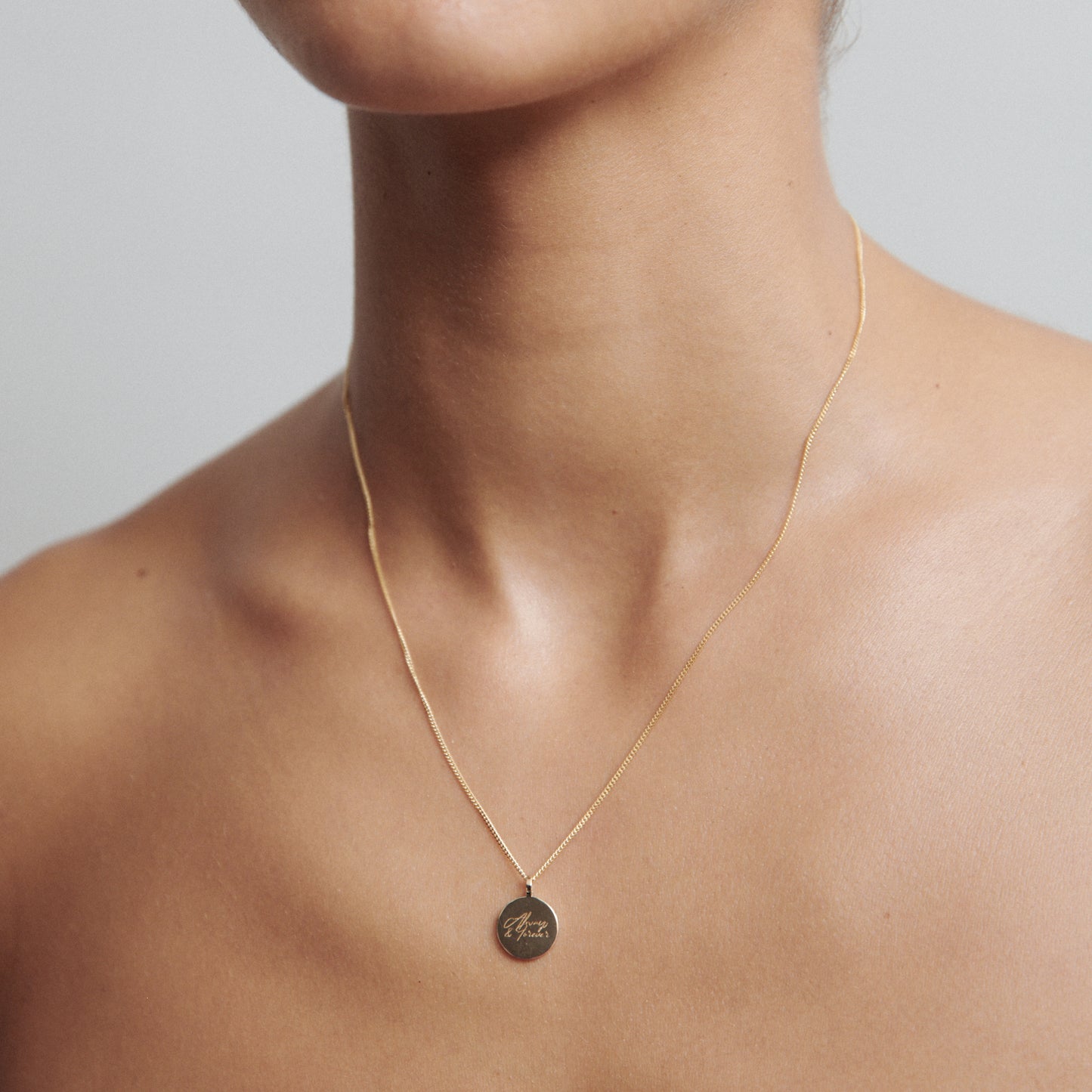Close-up of a person wearing a delicate gold necklace with a round pendant engraved with "Breathe," showcasing elegant, high-end jewellery.