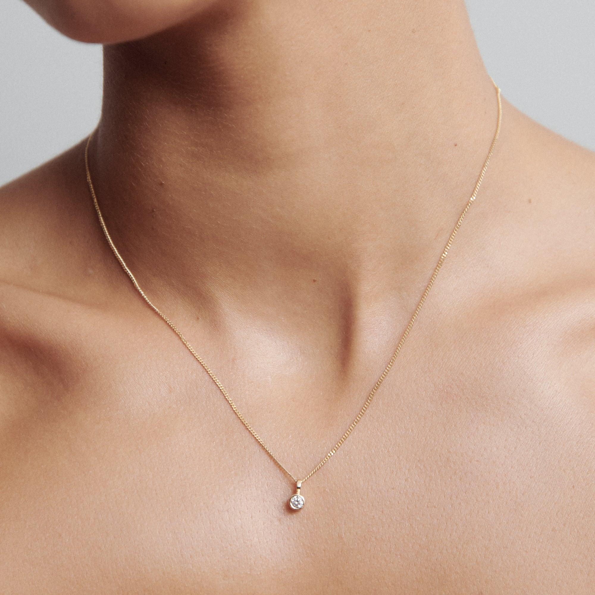A delicate gold chain necklace with a single diamond pendant adorning the neck, showcasing minimalist luxury jewellery design.