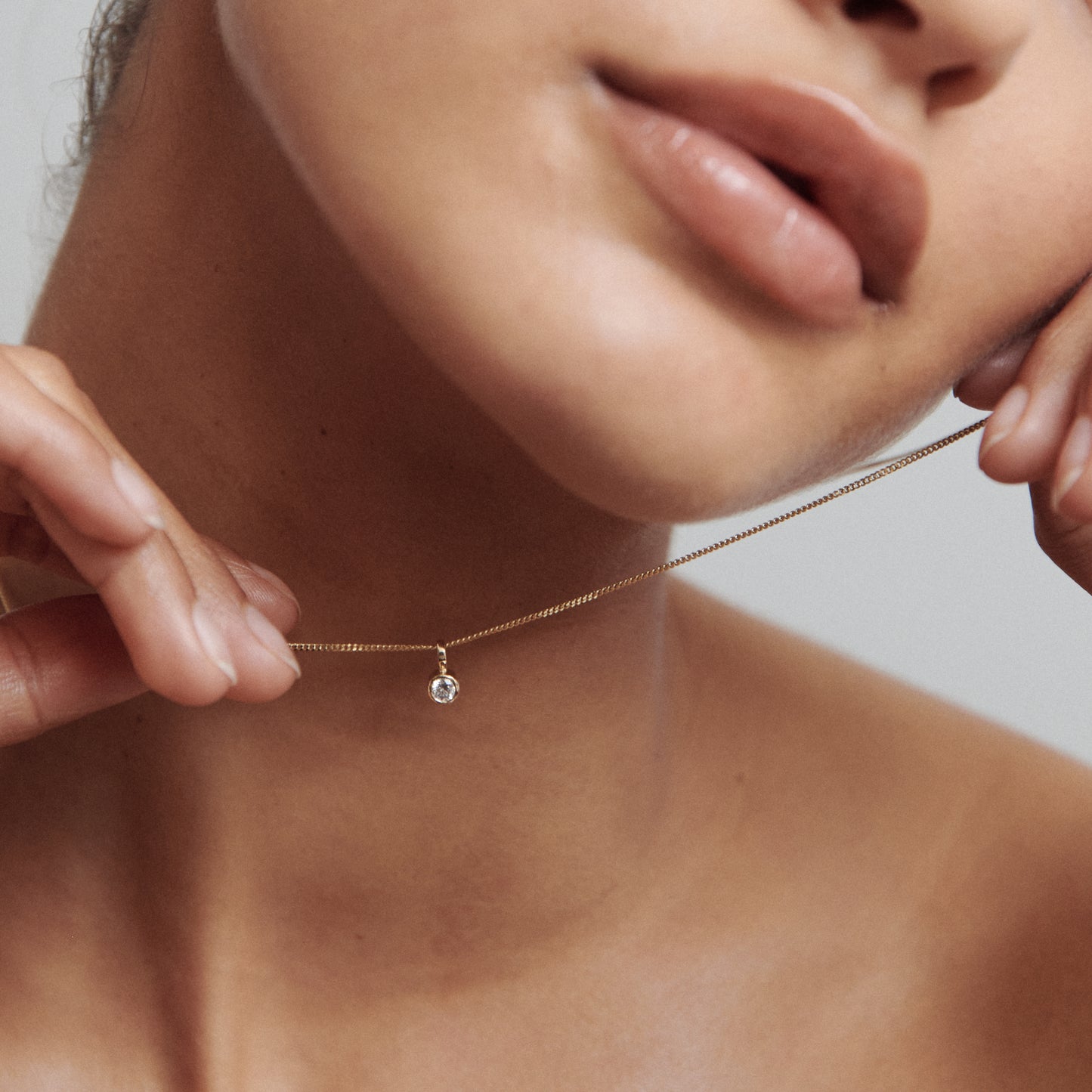 Close-up of a woman holding a delicate gold necklace with a small diamond pendant, highlighting luxury jewellery aesthetics.