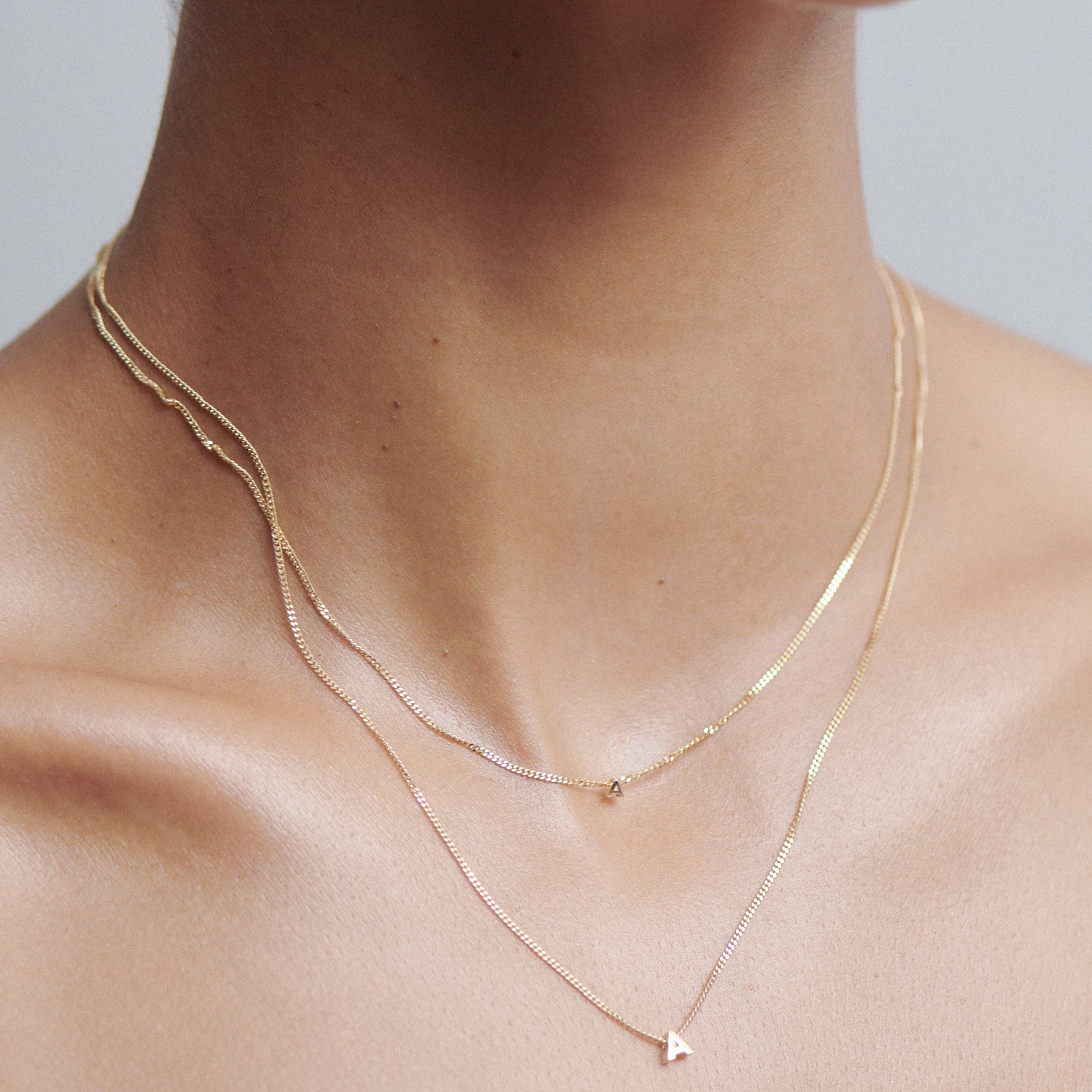 Close-up of a neck wearing three delicate gold necklaces, one featuring a small 'A' pendant. Perfect for luxury jewellery enthusiasts.