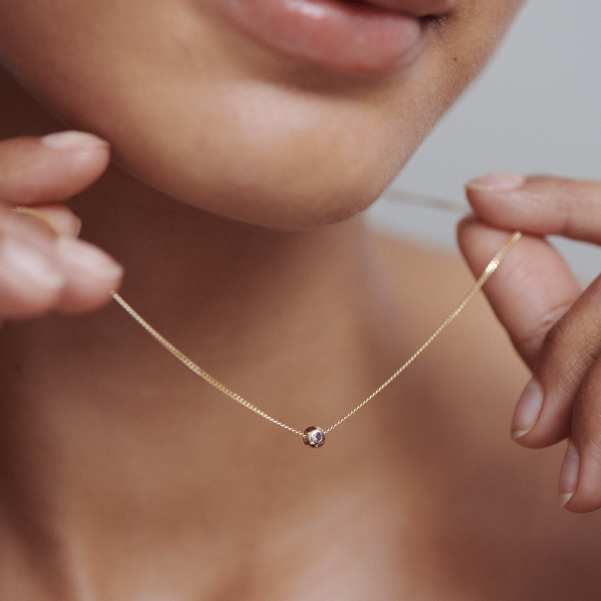 Close-up of a minimalist gold necklace with a single diamond pendant, elegantly held by a person, highlighting luxury jewellery details.