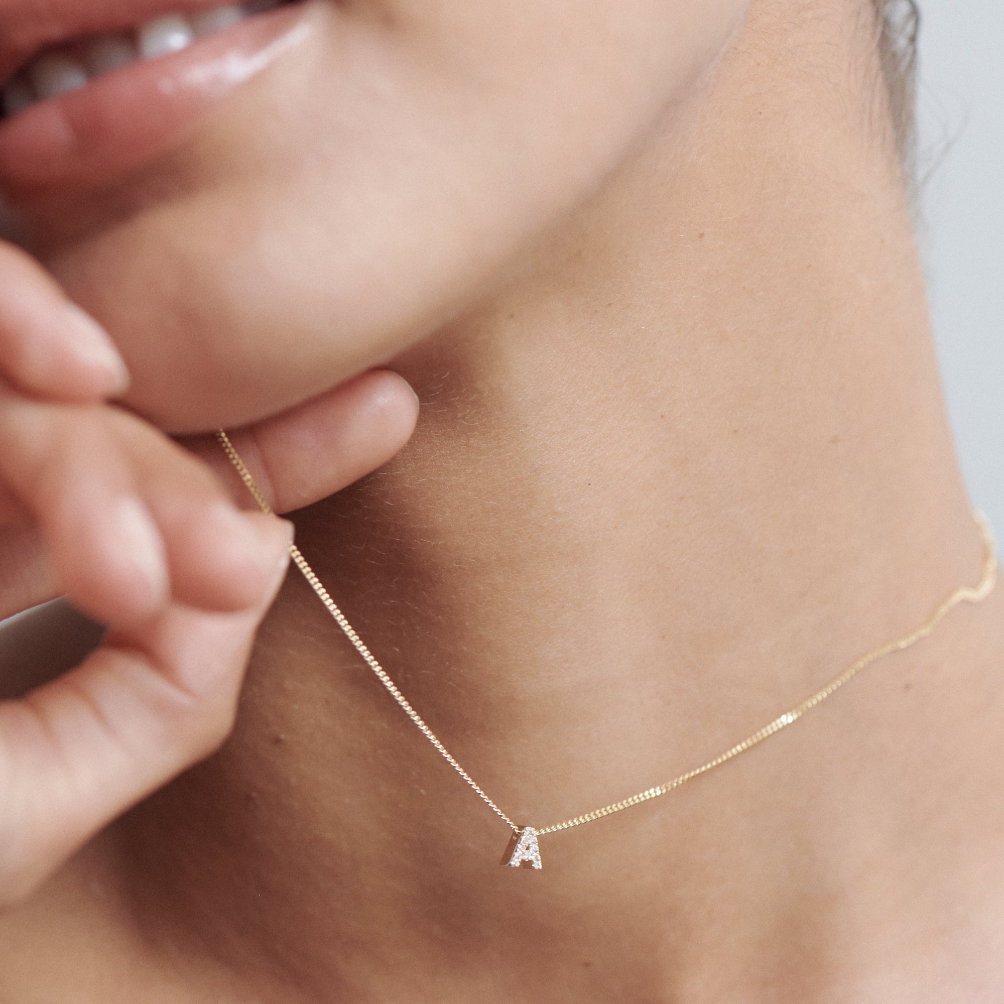 Close-up of a woman's neck wearing a delicate gold necklace with an initial "A" pendant. Luxurious minimalist jewellery style.
