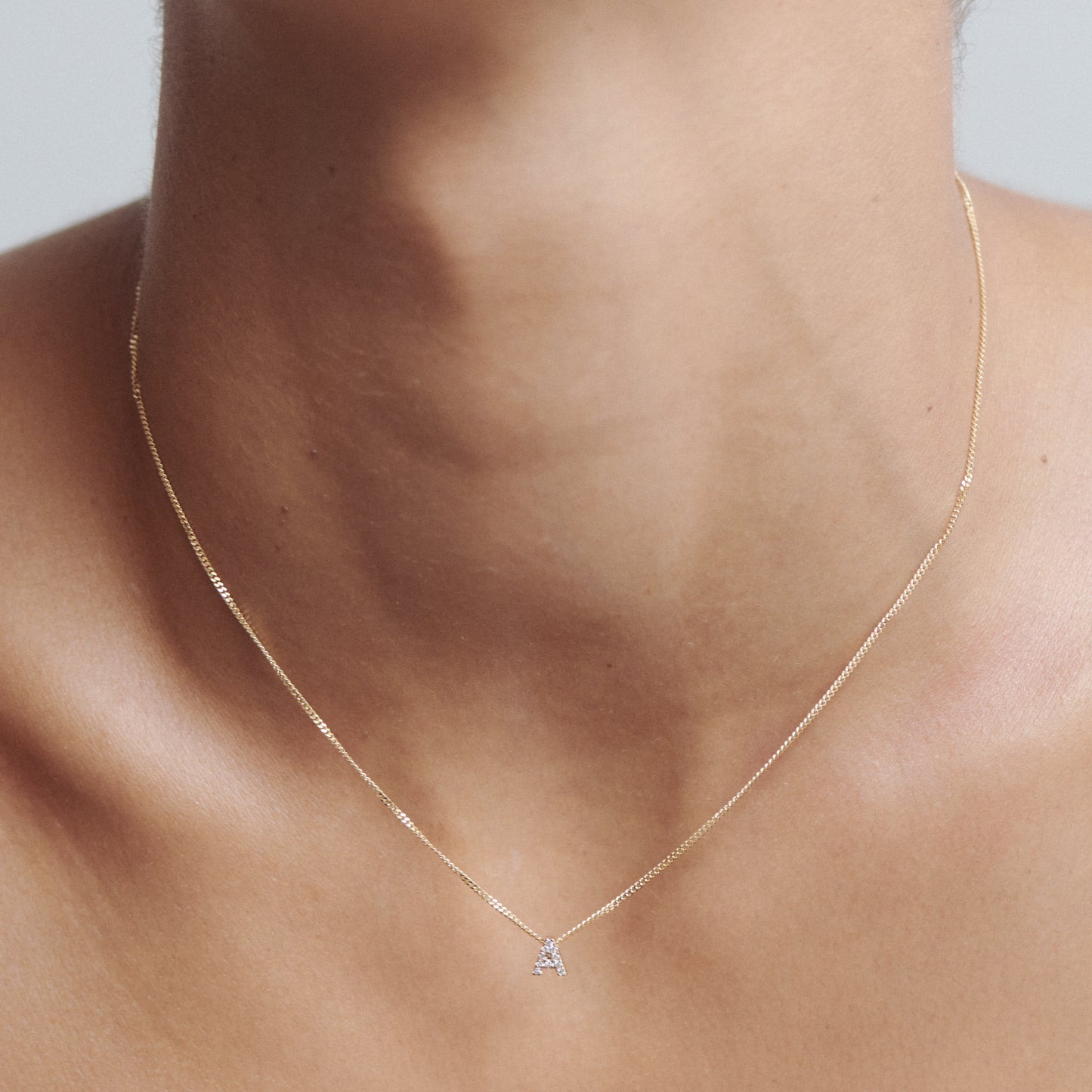 Close-up of a delicate gold necklace with a small triangle pendant on a person's neck. Minimalist and elegant luxury jewellery.
