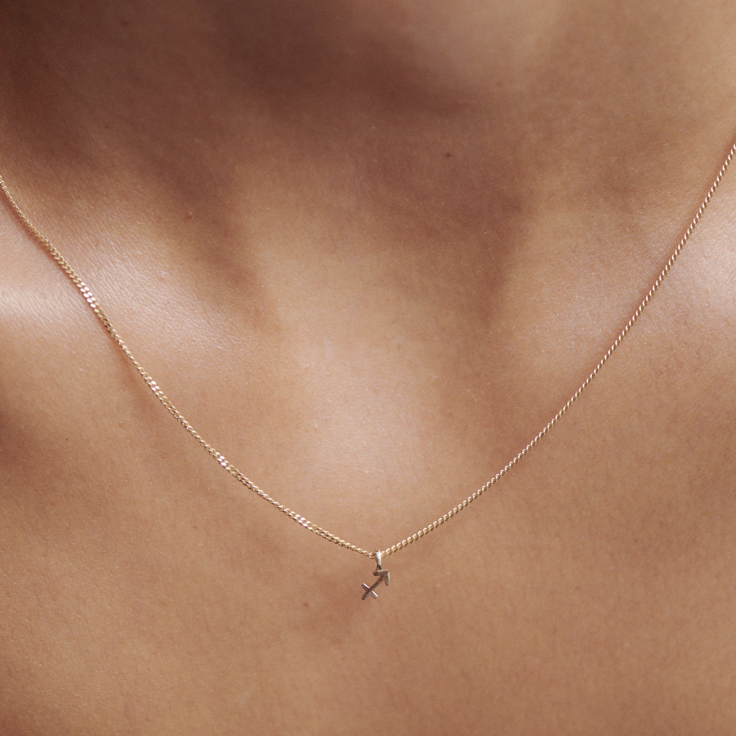 A delicate gold necklace with a small cross pendant rests on a person's collarbone, showcasing elegance and simplicity in luxury jewellery.