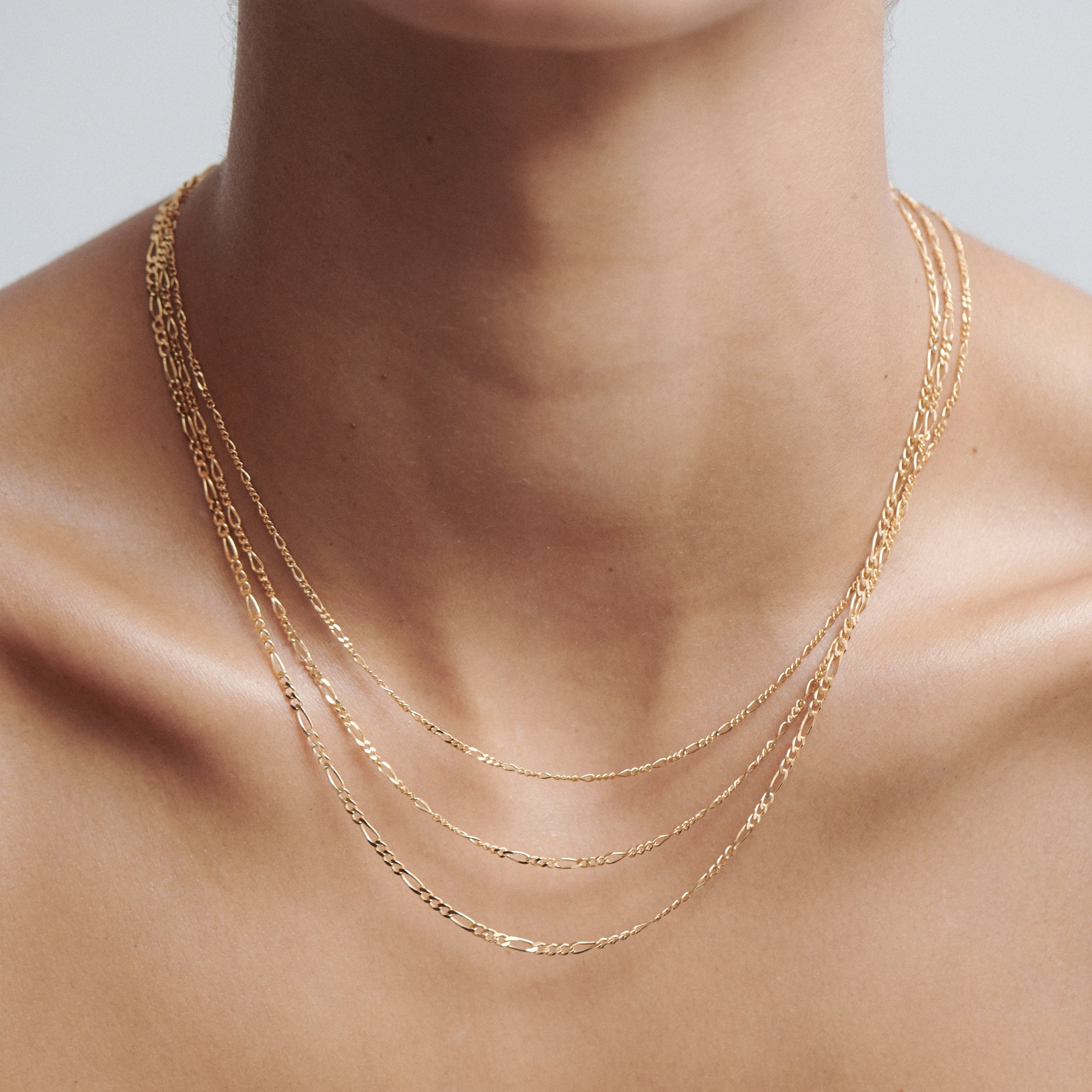 Close-up of a person wearing three delicate gold chains layered elegantly around the neck, showcasing luxury jewellery fashion.