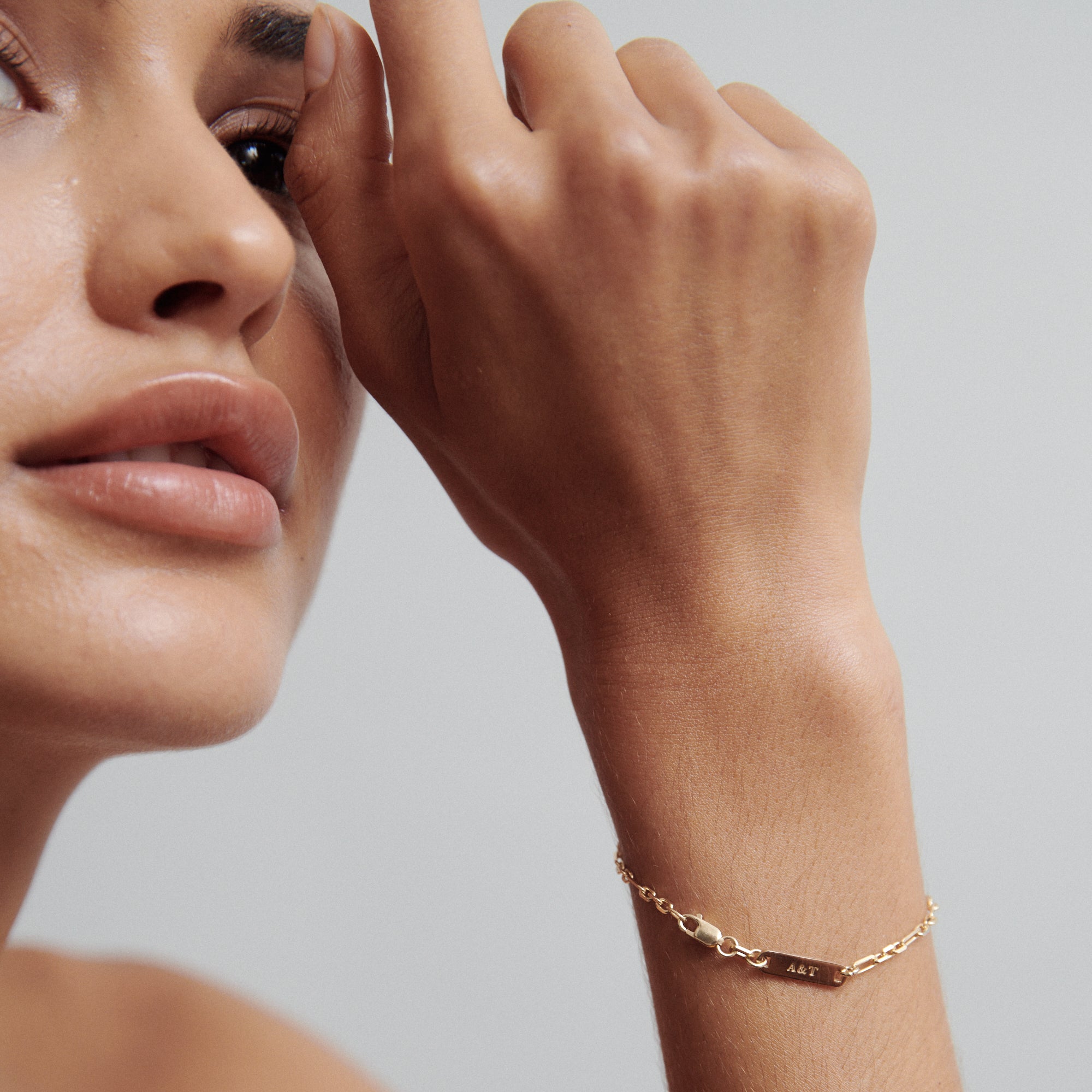 Woman's hand wearing a gold bracelet with "A&Z" inscription, close-up on face and jewellery, highlighting luxury and elegance.