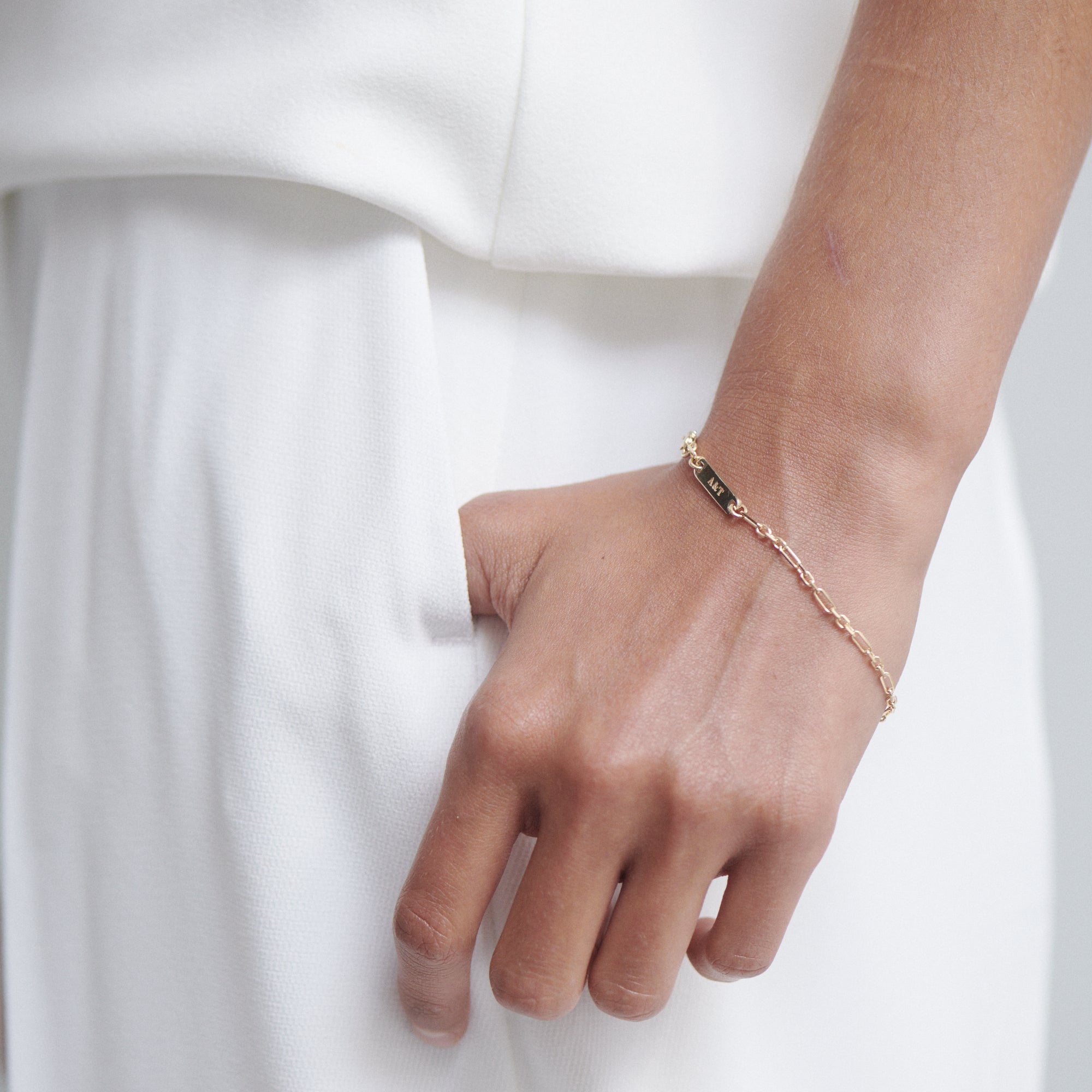 A delicate gold bracelet adorns a wrist, paired with an elegant white outfit, highlighting luxury jewellery and minimalist fashion.
