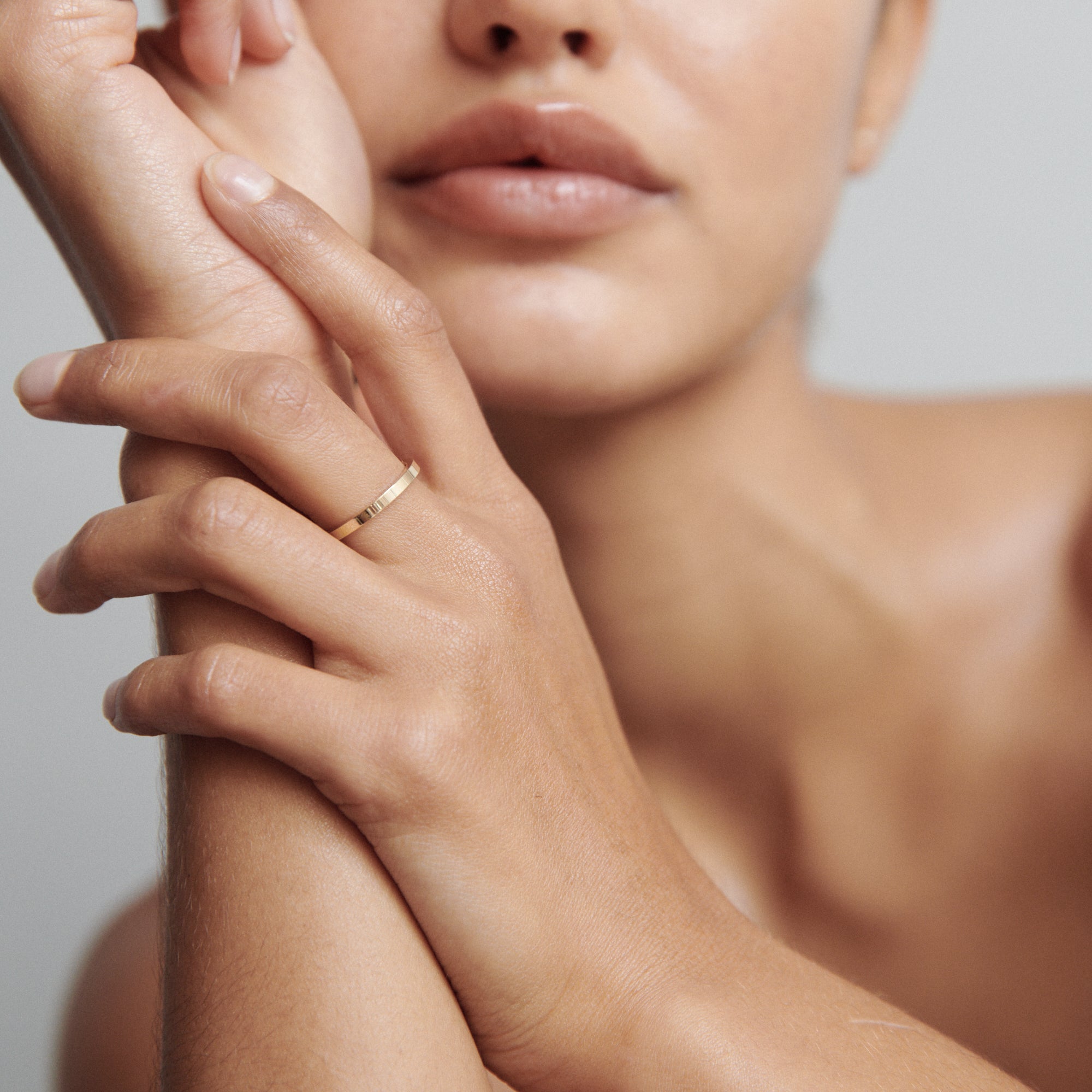 Close-up of a woman wearing a simple gold ring on her left hand, resting on her chin. Minimalist luxury jewellery aesthetic.